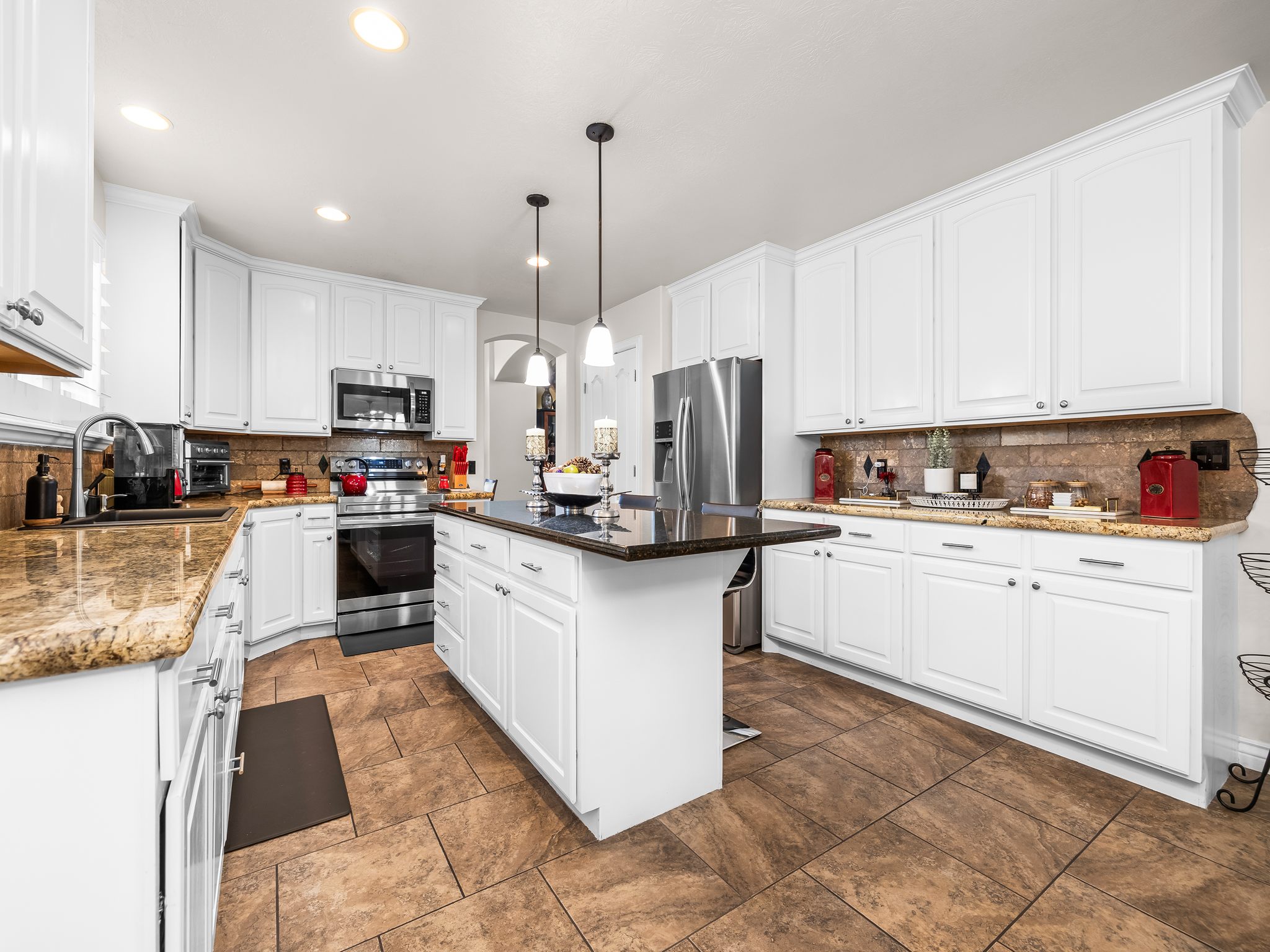 Spacious kitchen featuring an expansive center island with dark countertop, white cabinetry with silver hardware, stainless steel appliances, and a tiled floor