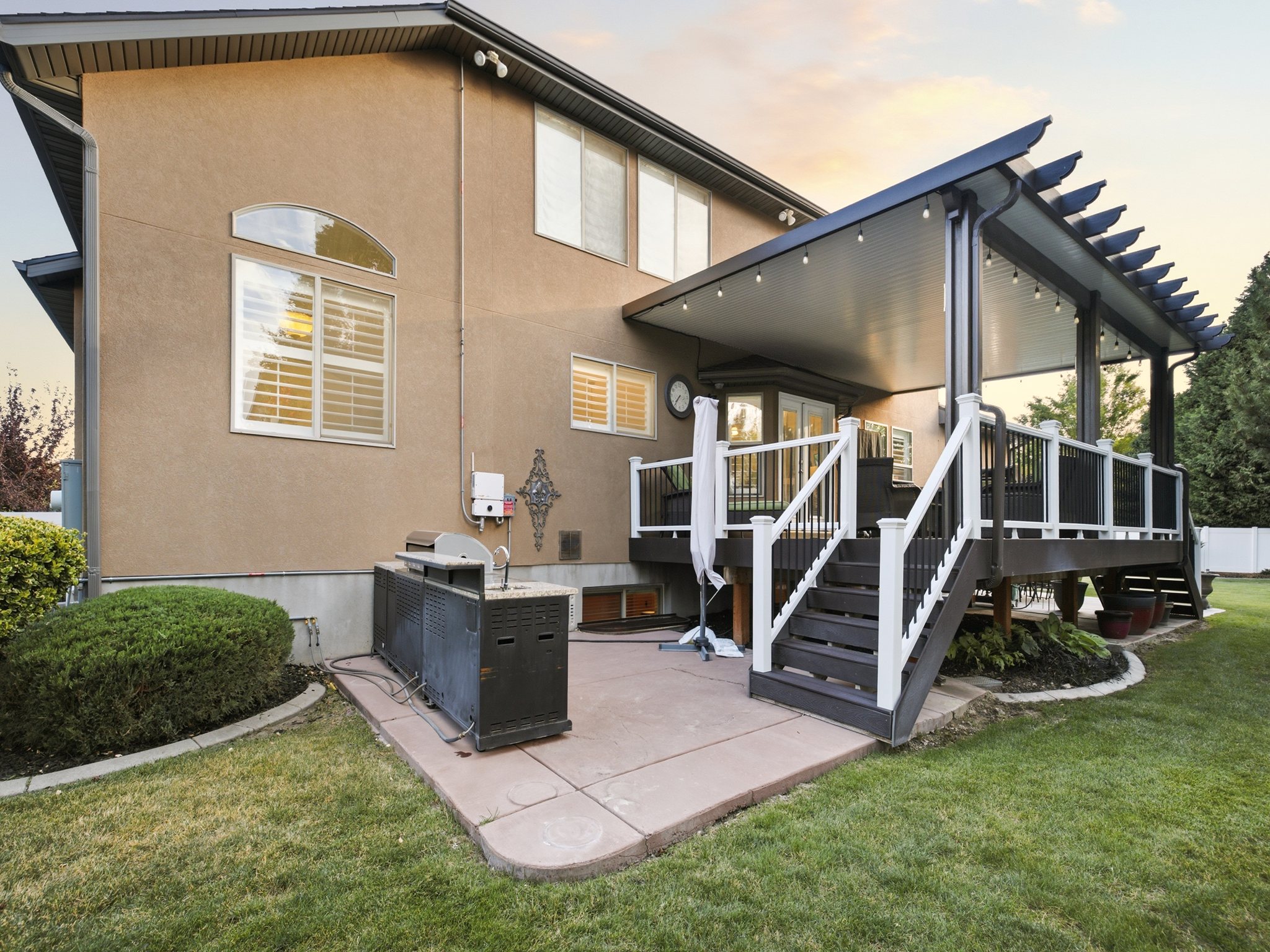 Expansive rear yard featuring a covered deck with pergola details, concrete patio, and built-in outdoor kitchen