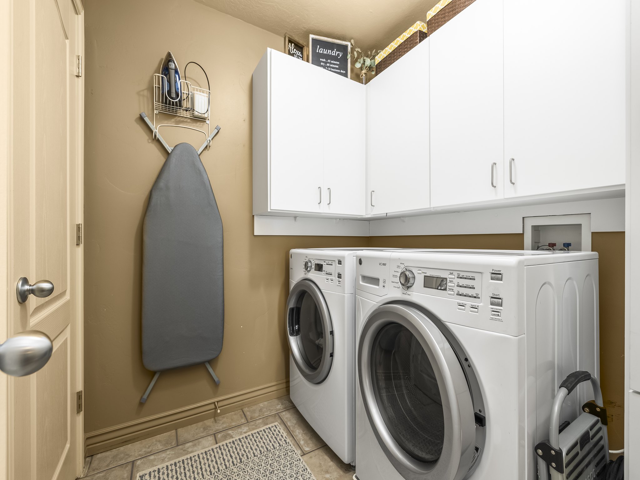 Dedicated laundry area featuring tiled flooring, upper white cabinetry, and light tan walls