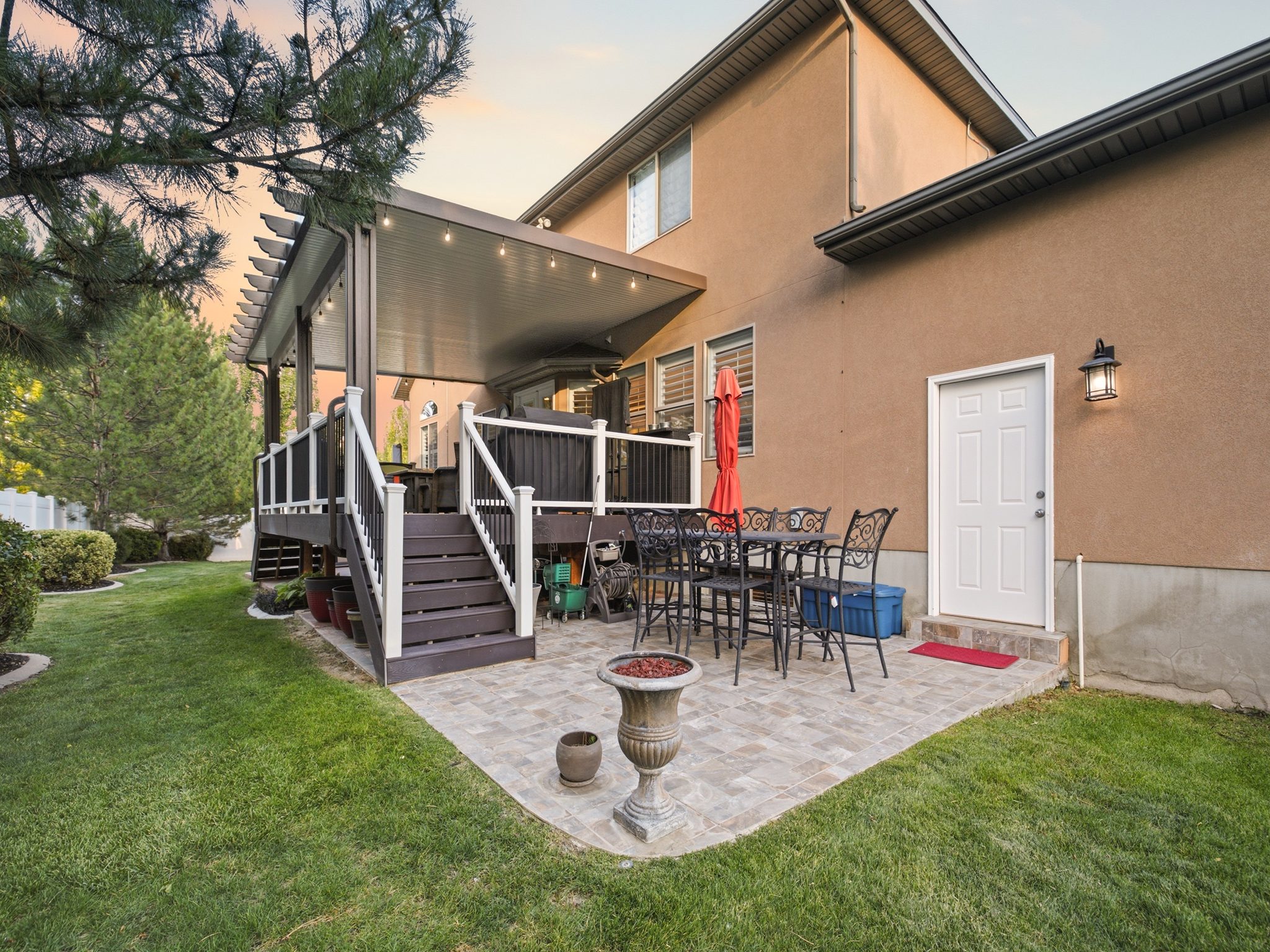 Rear exterior featuring a covered deck with pergola detailing, paver patio, and a manicured lawn