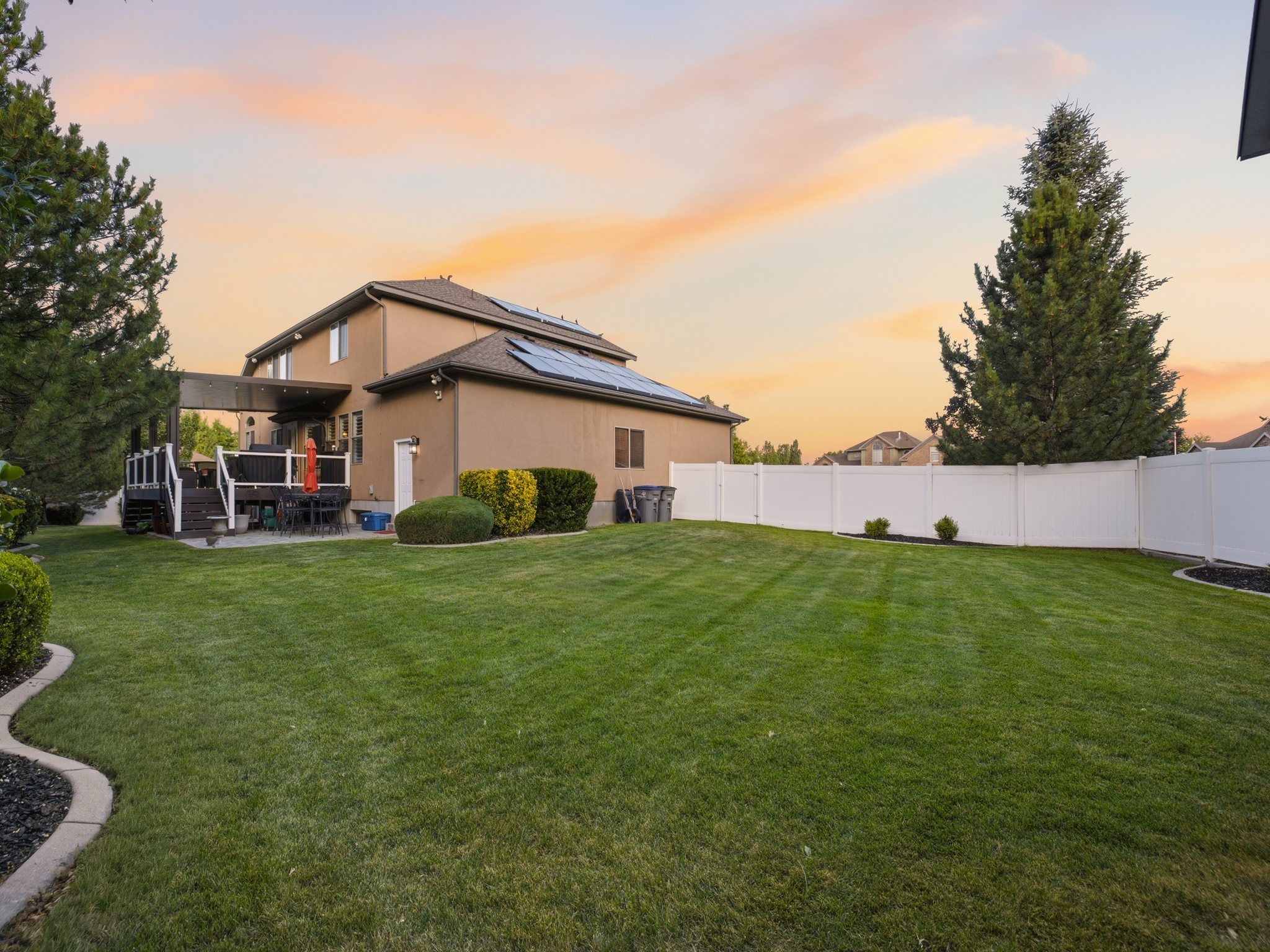 Expansive backyard featuring a manicured lawn, established landscaping, and a white privacy fence