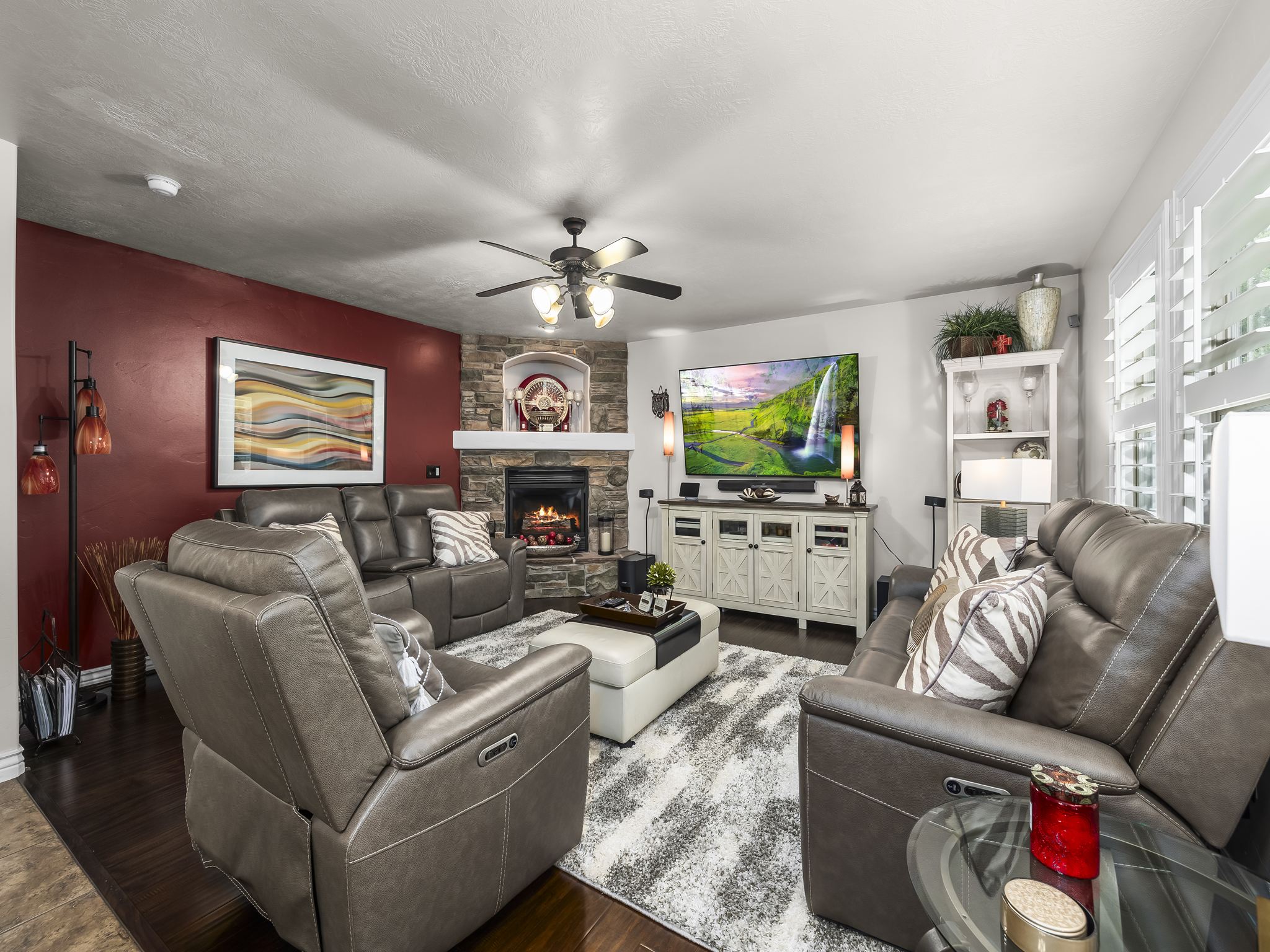Living room featuring a stone-clad fireplace with a mantel, dark wood-finish flooring, and white plantation shutters