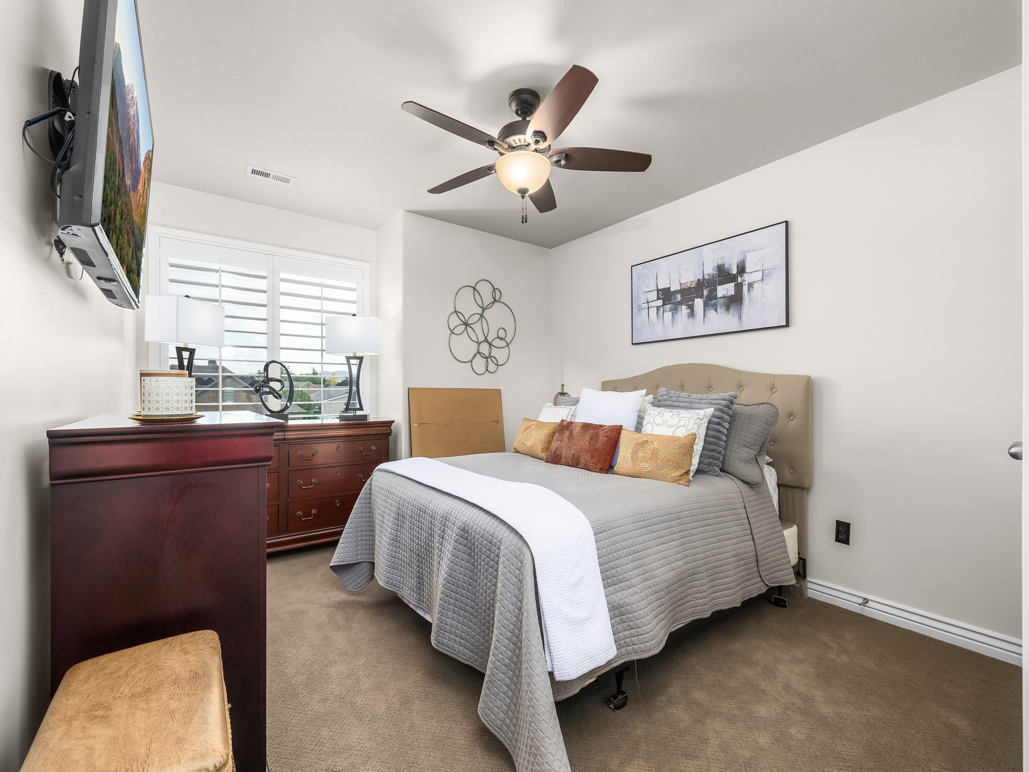 Carpeted bedroom featuring a ceiling fan with integrated lighting, a window with white plantation shutters, and light-toned walls