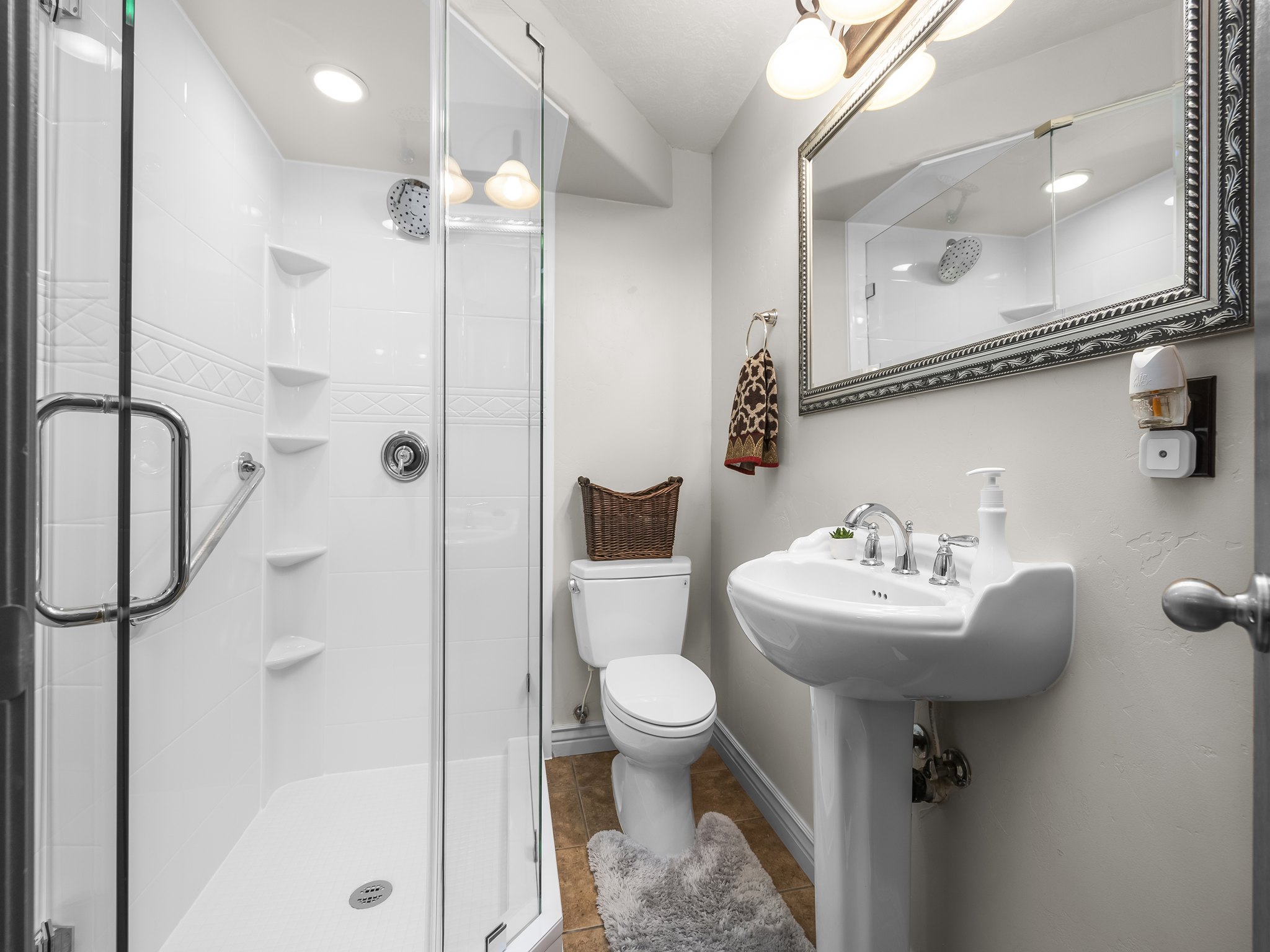 Bathroom featuring a glass-enclosed shower with integrated shelving, a pedestal sink with chrome fixtures, and a decorative framed mirror