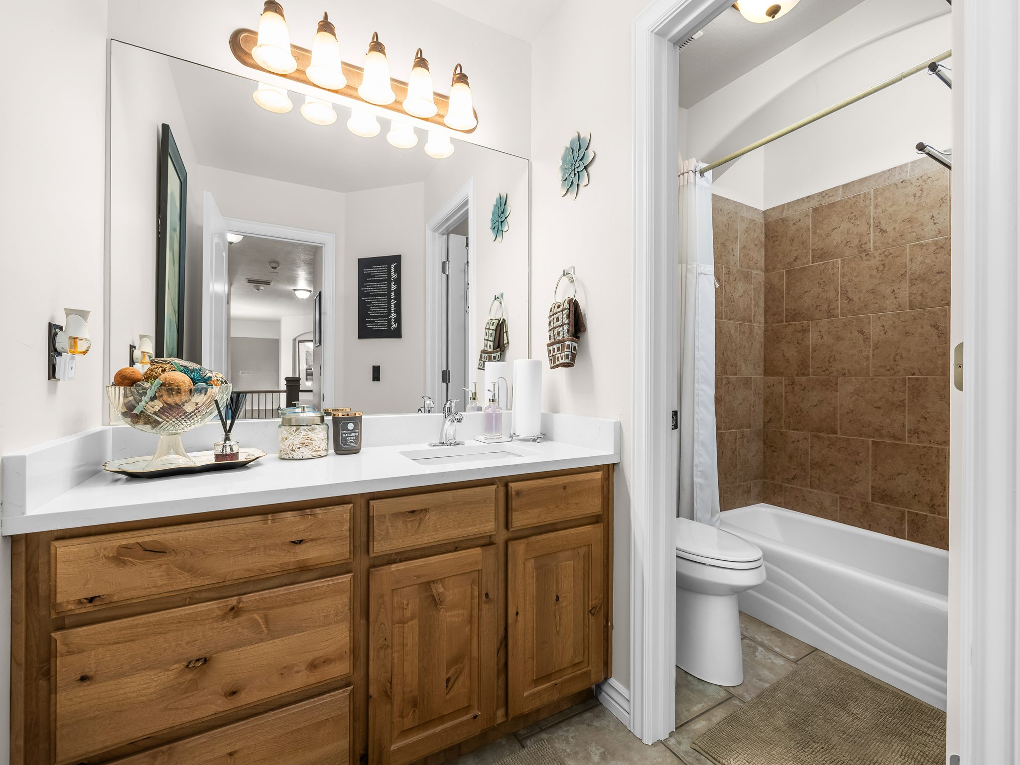 Bathroom featuring a single vanity with wood-finish cabinetry, a light-toned countertop, and a large wall-mounted mirror
