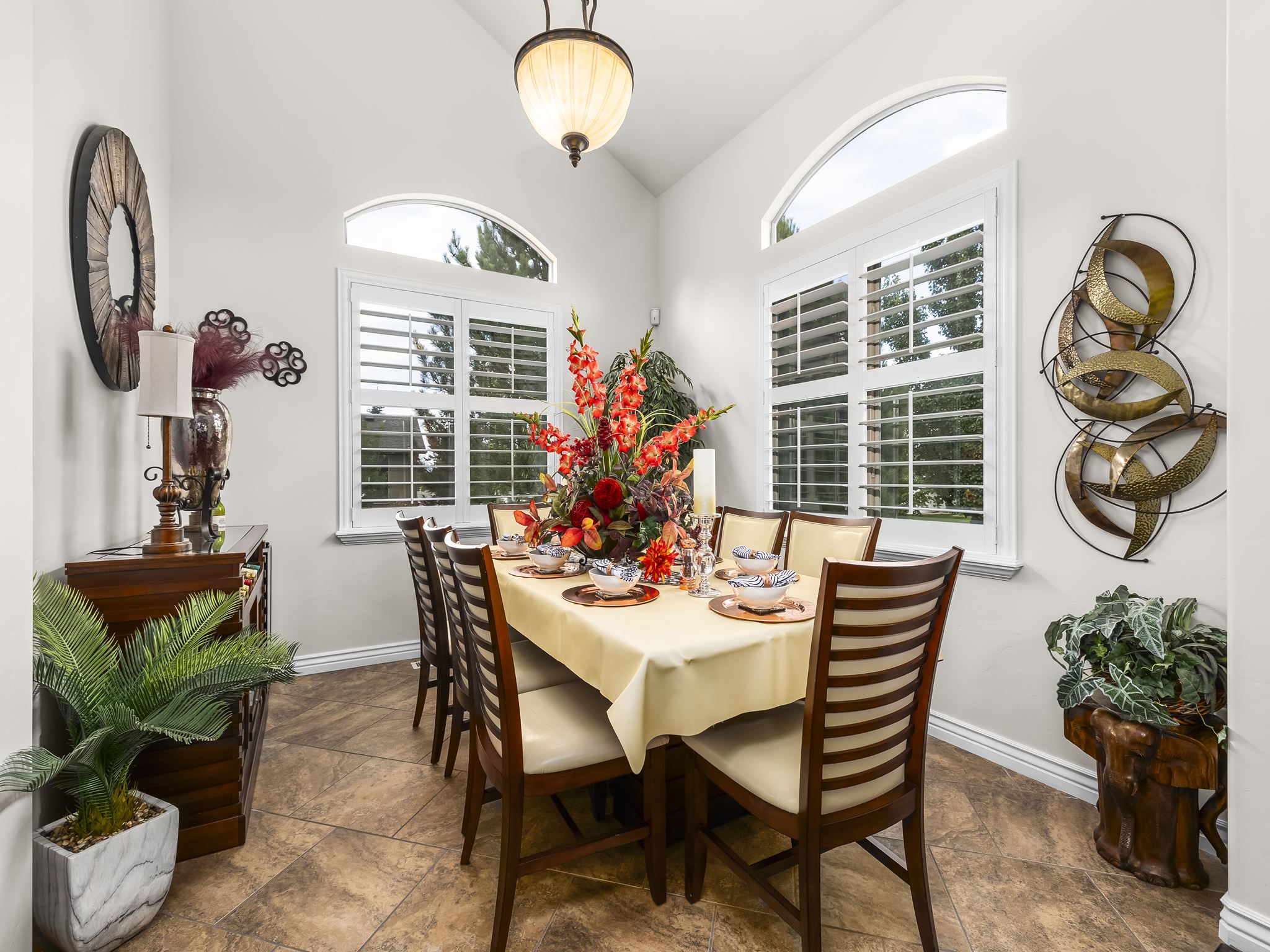 Vaulted ceiling dining area featuring two arched windows with plantation shutters, tile flooring, and a central pendant light fixture