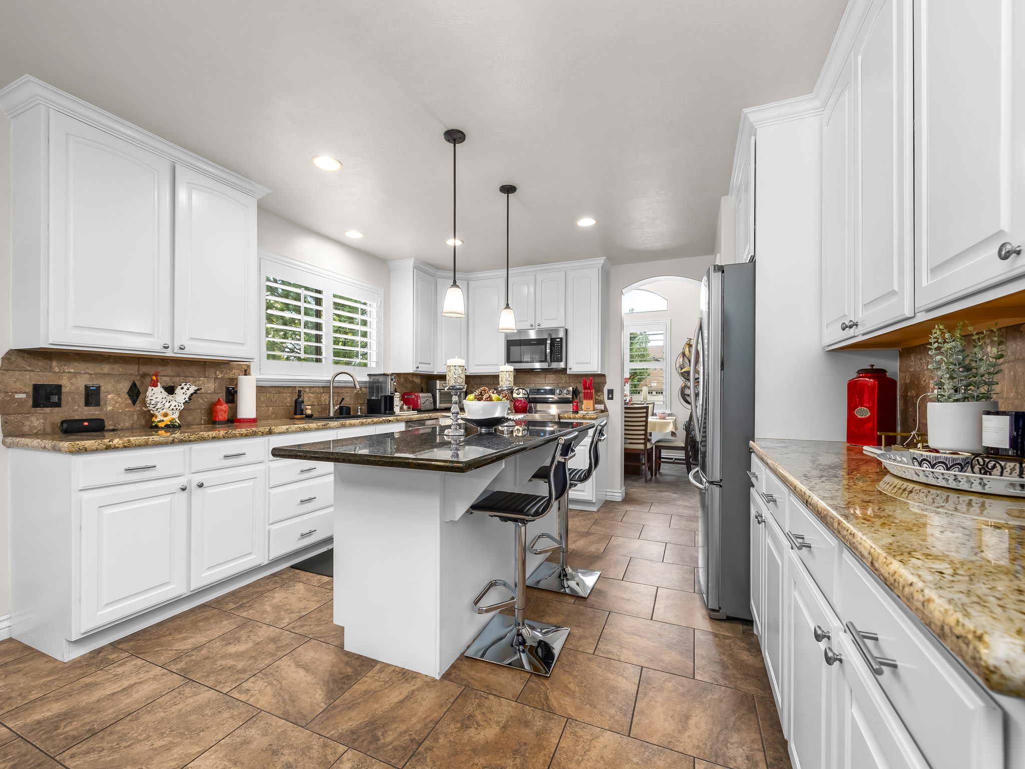 Kitchen featuring white cabinetry, granite countertops, an island with pendant lighting, a stainless steel refrigerator, and wood-finish tile flooring