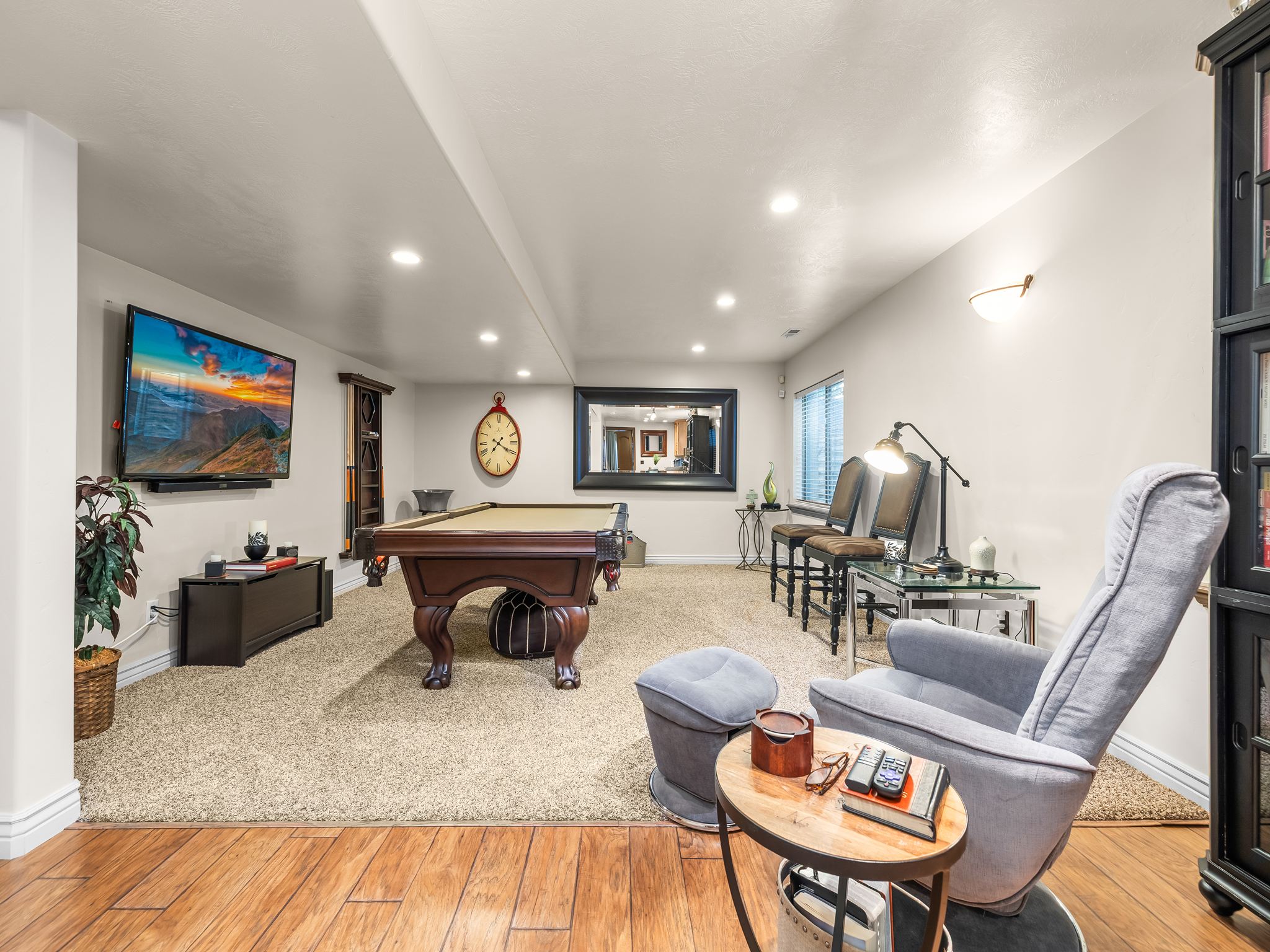 Spacious recreational area featuring wood-finish flooring, recessed lighting, and a neutral carpeted zone