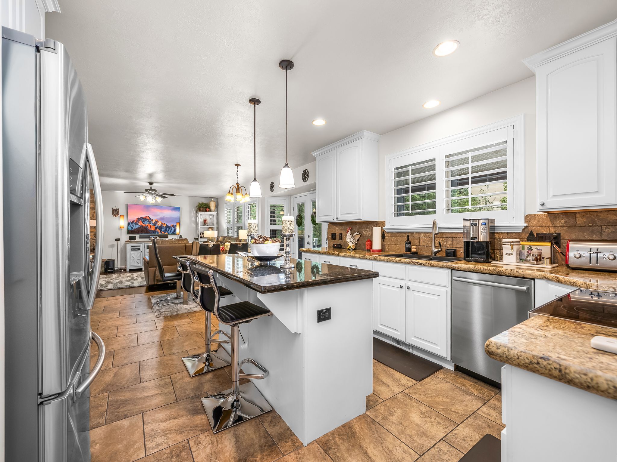 Spacious kitchen featuring an island with pendant lighting, white cabinetry, granite countertops, and stainless steel appliances