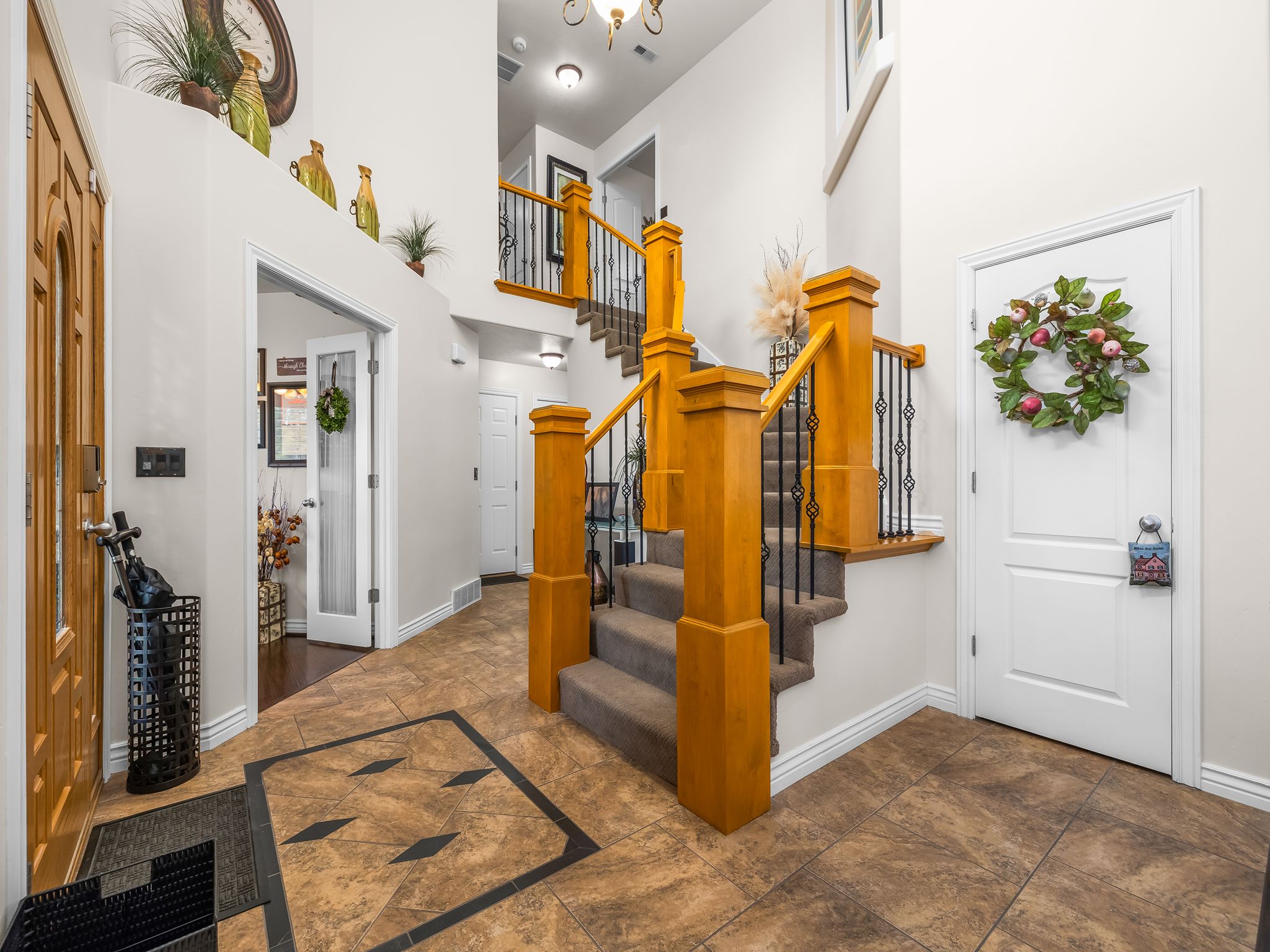 Two-story entryway featuring tile flooring with decorative inlay, a wood-finish staircase with carpeted treads, and wrought iron balusters
