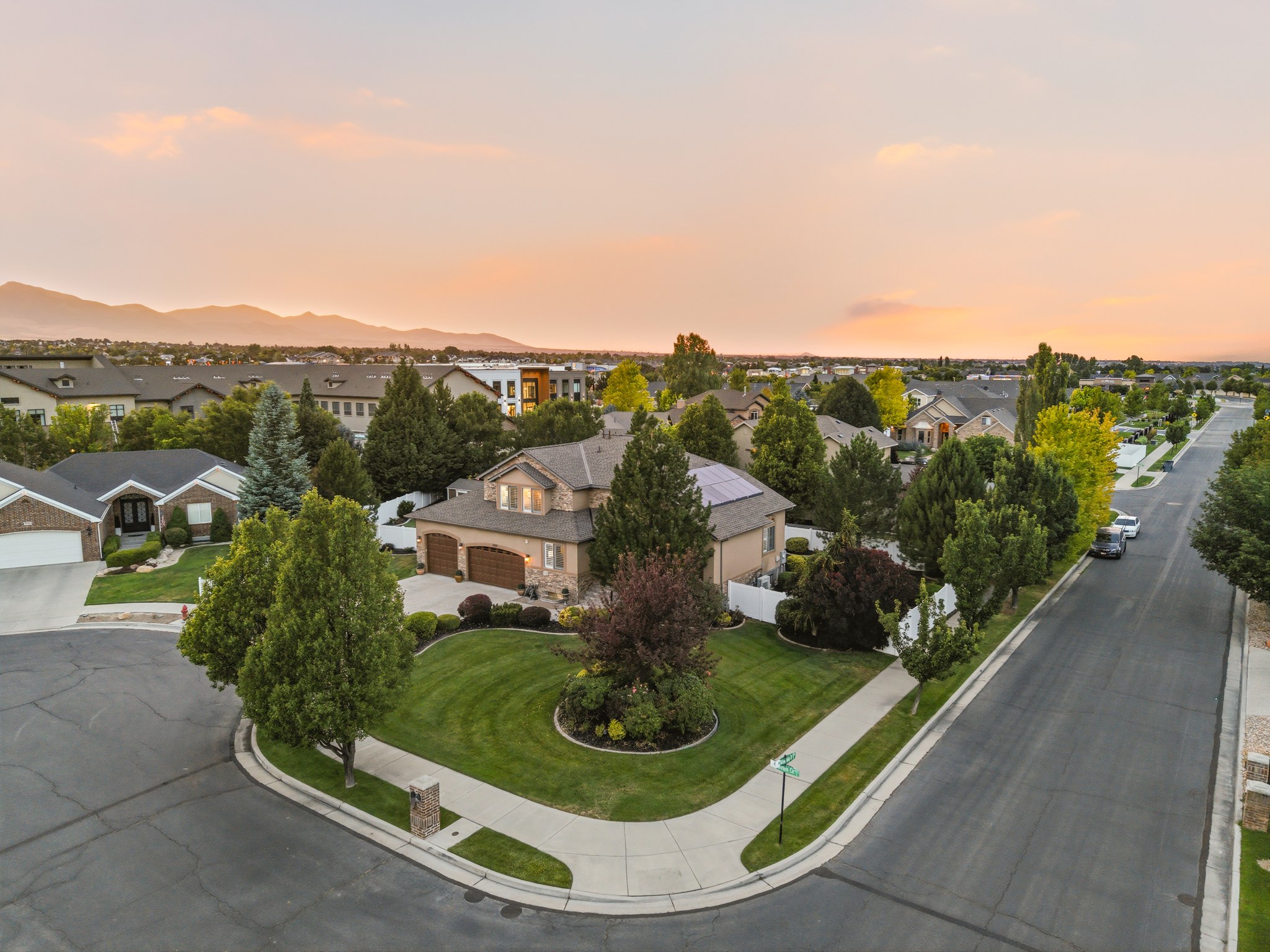 Large corner lot featuring a stucco and stone exterior, mature landscaping, a two-car garage, and solar panels