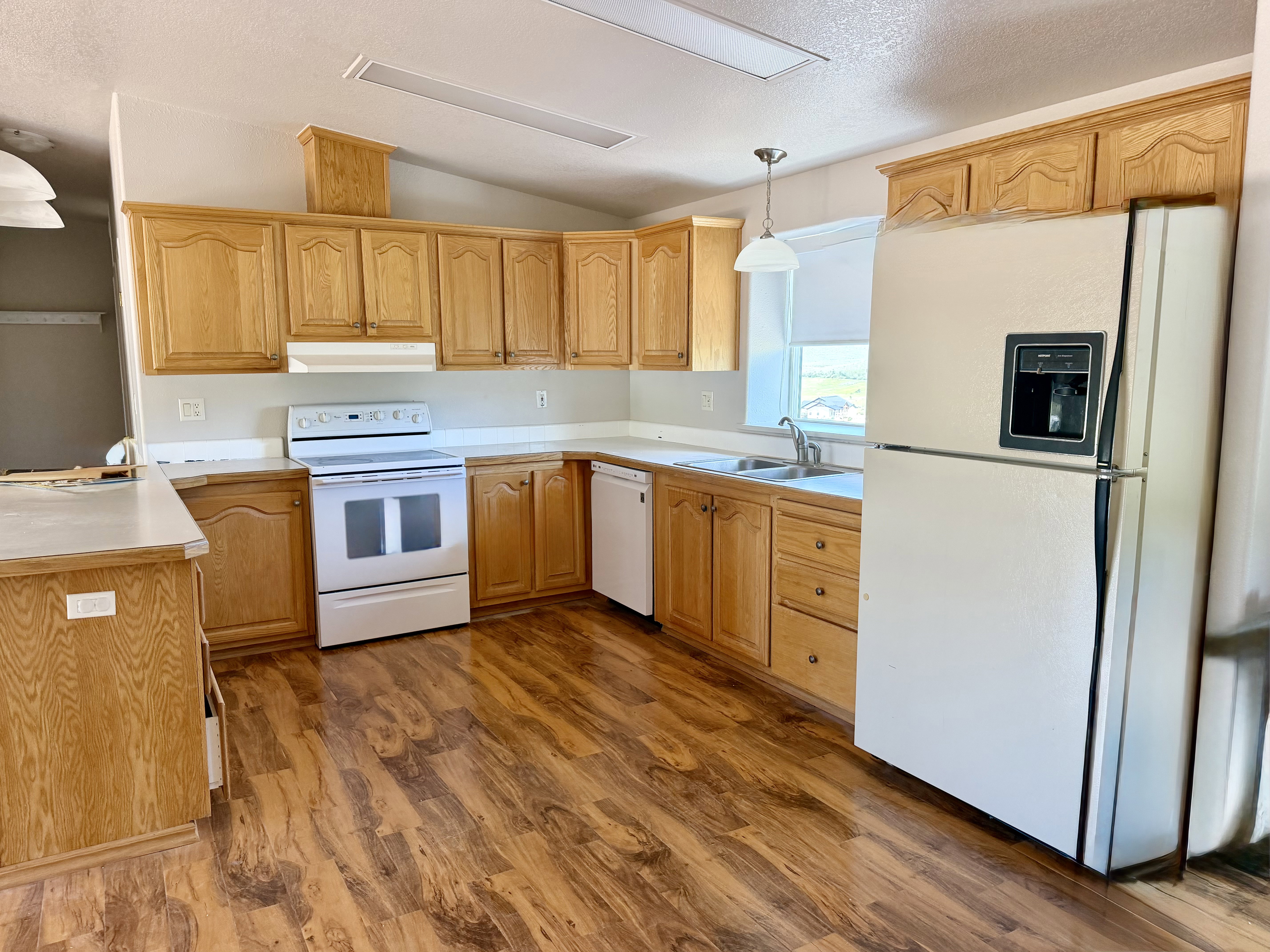 Kitchen featuring wood-finish flooring, light wood cabinetry, white countertops, a white electric range, and a white refrigerator with an ice and water dispenser