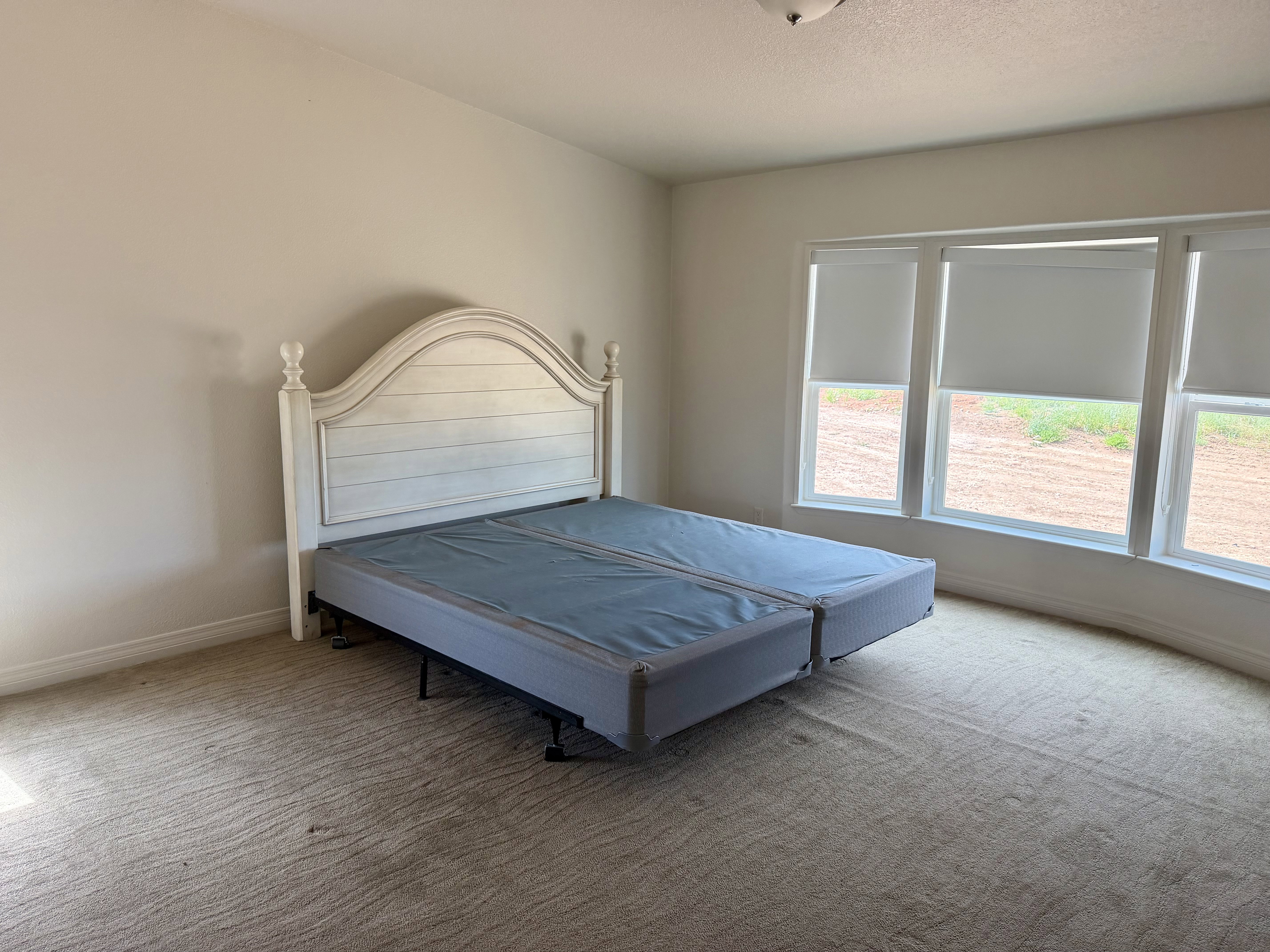 Bright room featuring light-colored carpet, white walls, and a multi-pane window with roller shades
