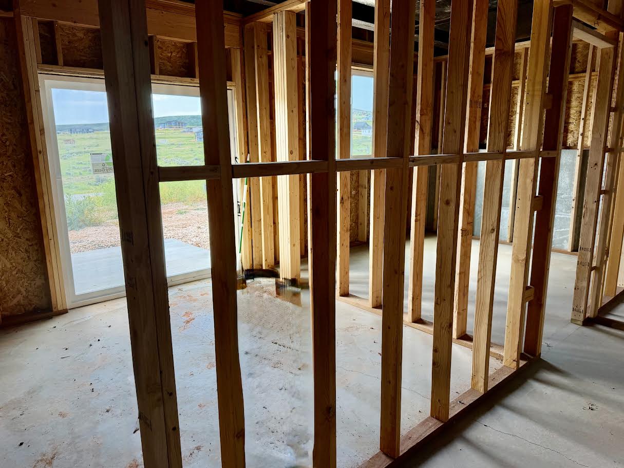 Unfinished interior framing with exposed wood studs, concrete flooring, and multiple window openings