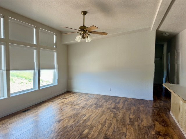 Spacious room featuring wood-finish flooring, a contemporary ceiling fan, and large windows with roller shades