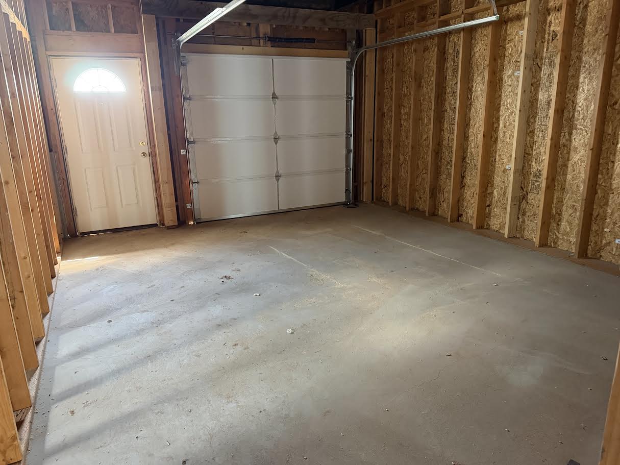 Spacious garage with a concrete floor, a white overhead door, and an insulated pedestrian door featuring an arched window