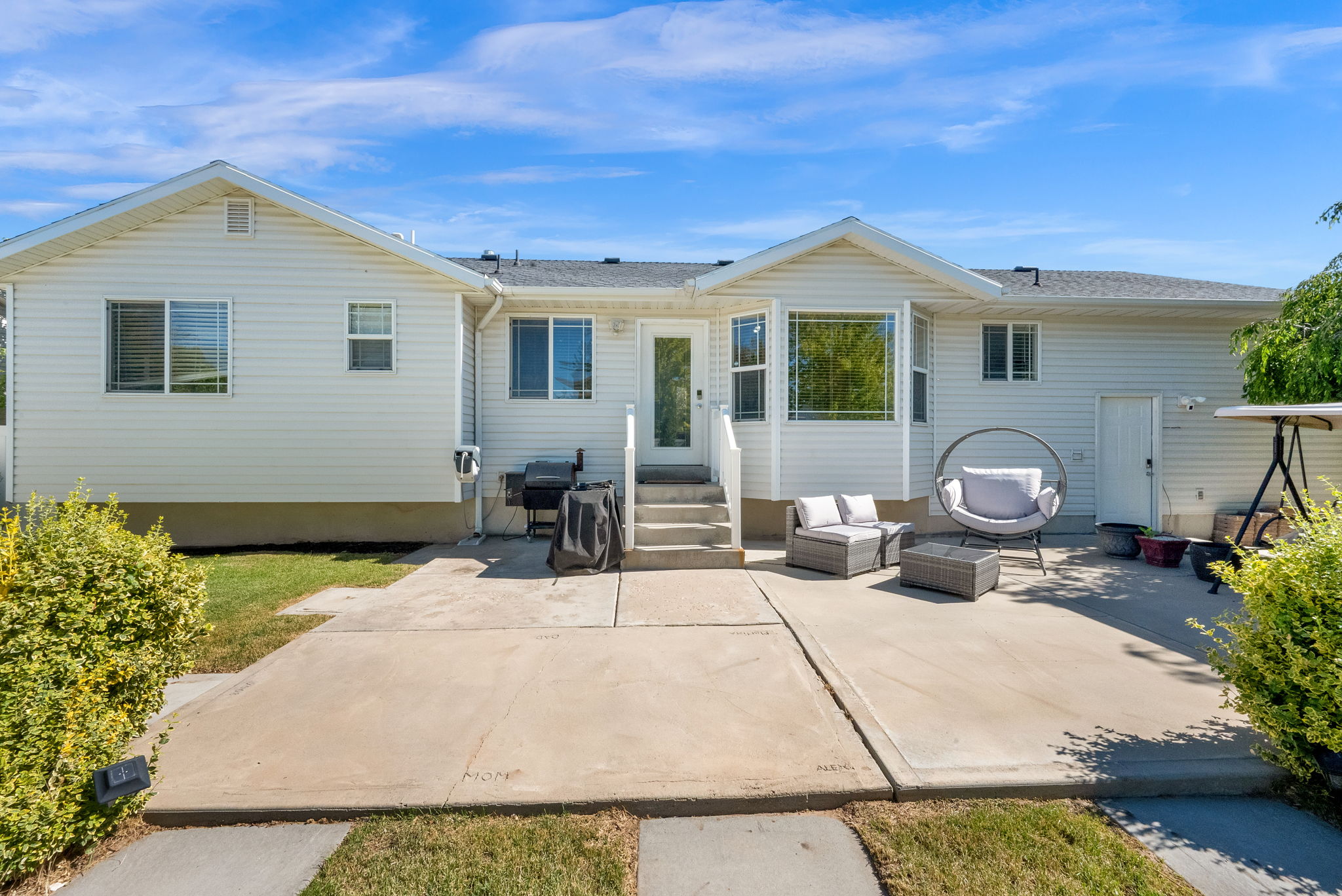 Rear exterior featuring a spacious concrete patio, light-colored siding, multiple windows, and a bay window