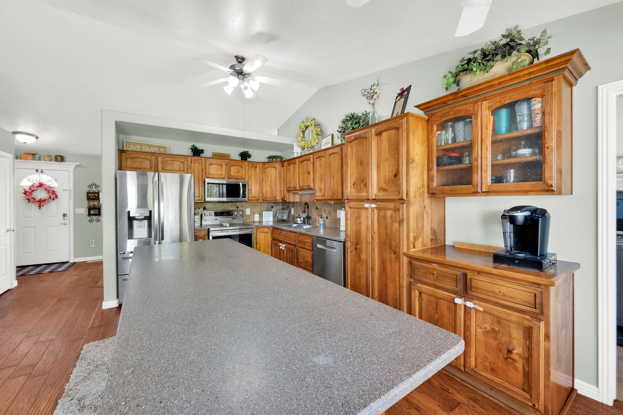 Kitchen featuring wood-finish flooring, a large island with a stone-finish countertop, wood cabinetry, stainless steel appliances, and vaulted ceilings