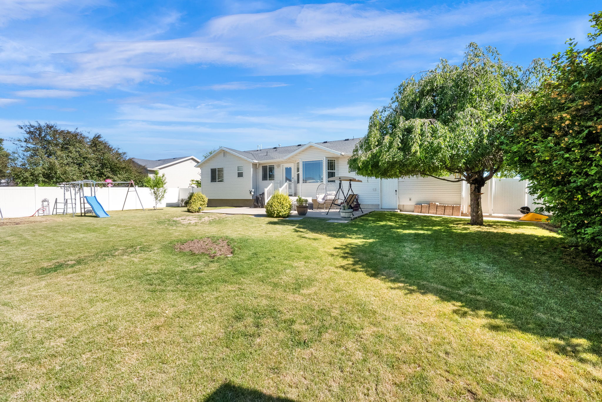 Expansive backyard featuring a large green lawn, mature trees, and a white privacy fence