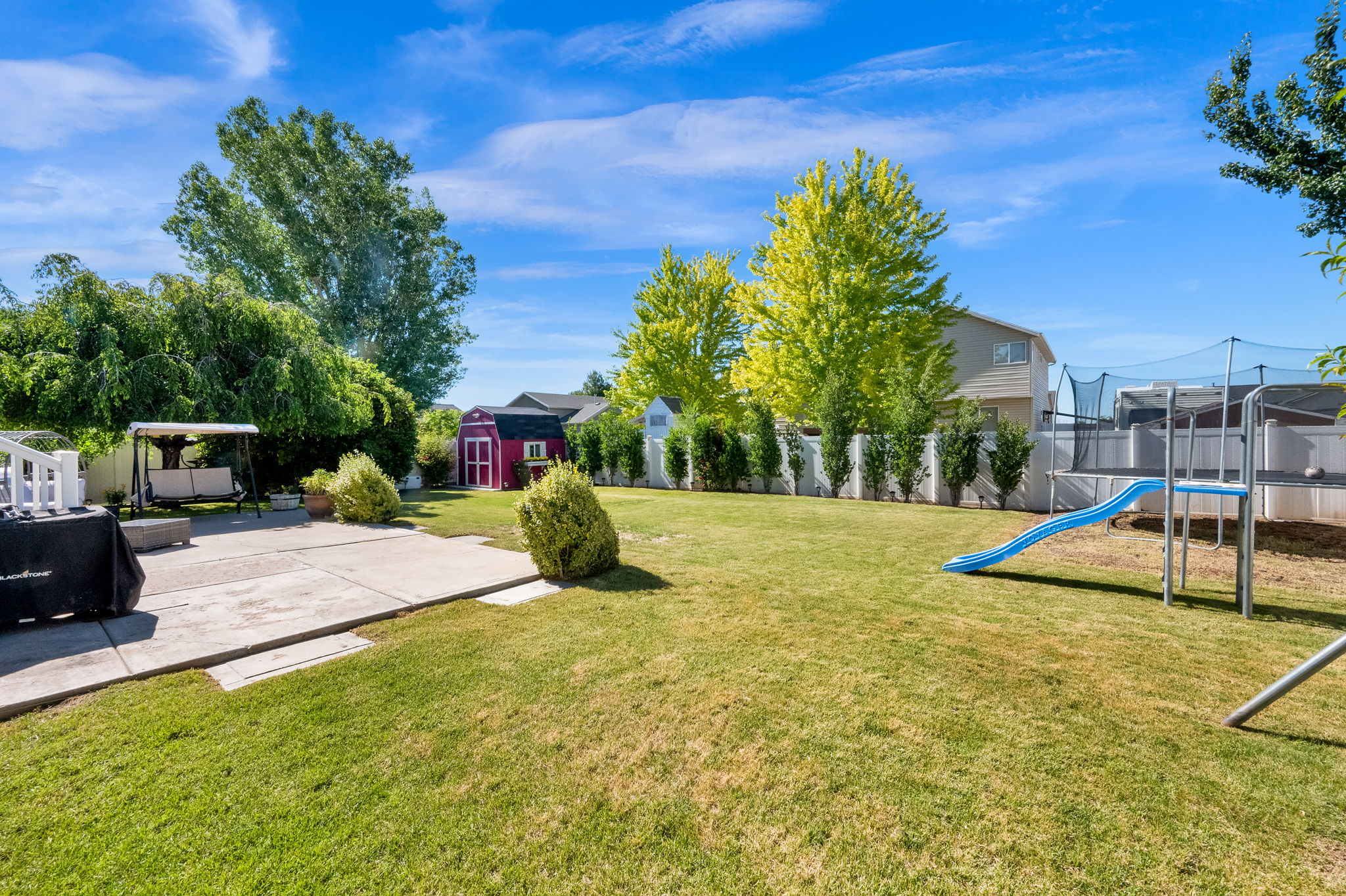 Expansive backyard featuring a manicured lawn, a concrete patio, a vibrant red storage shed, and a privacy fence