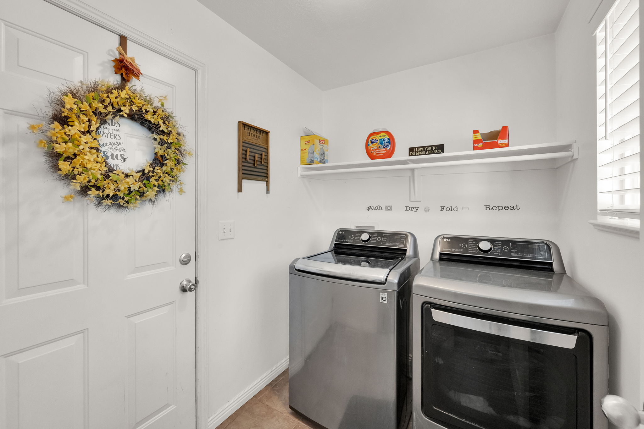 Laundry area featuring a built-in wall shelf, a window with blinds, and durable tile flooring