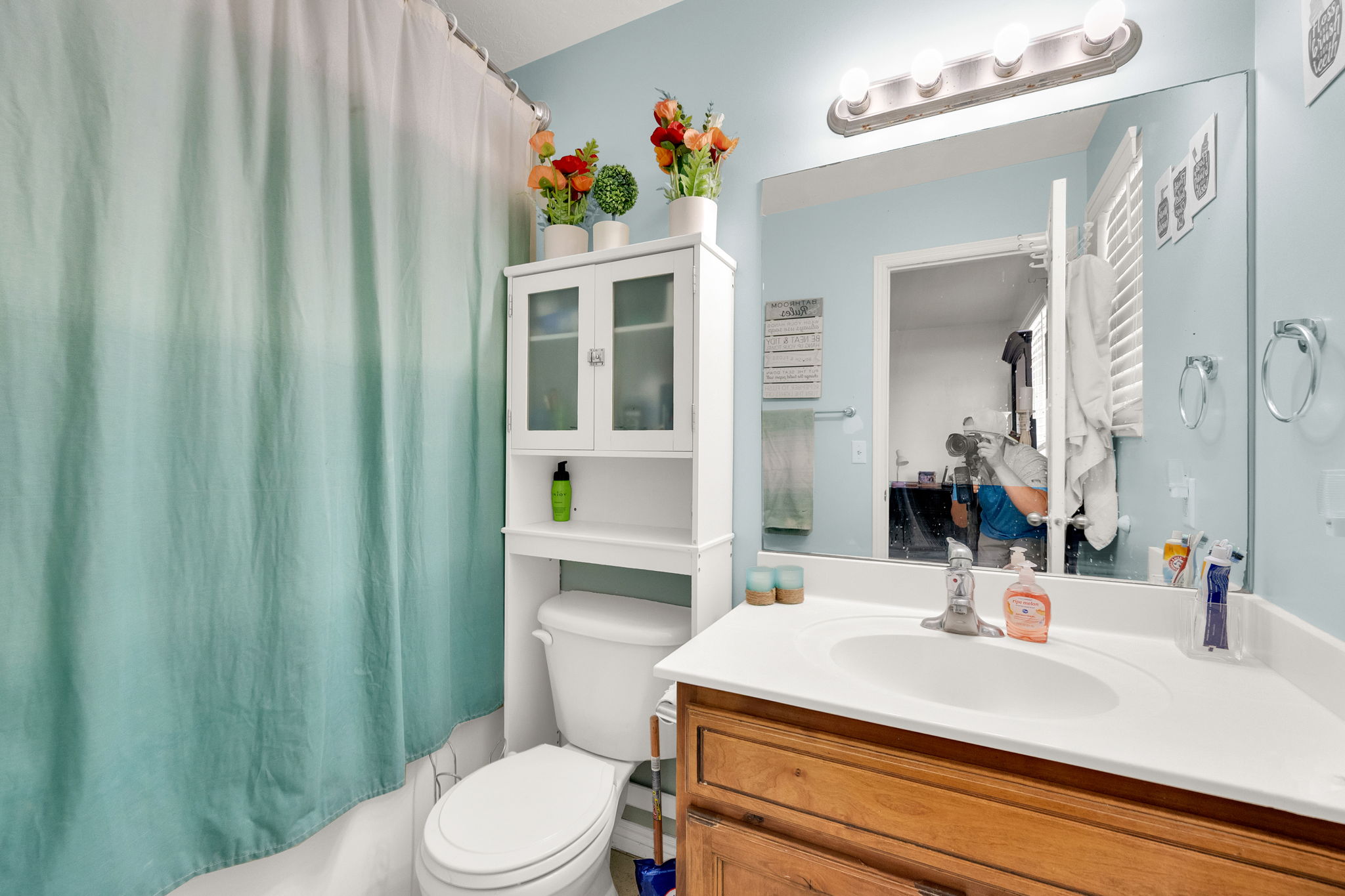 Bathroom featuring a white elongated toilet, wood-finish vanity with an integrated white sink, and a large mirror with a four-light fixture