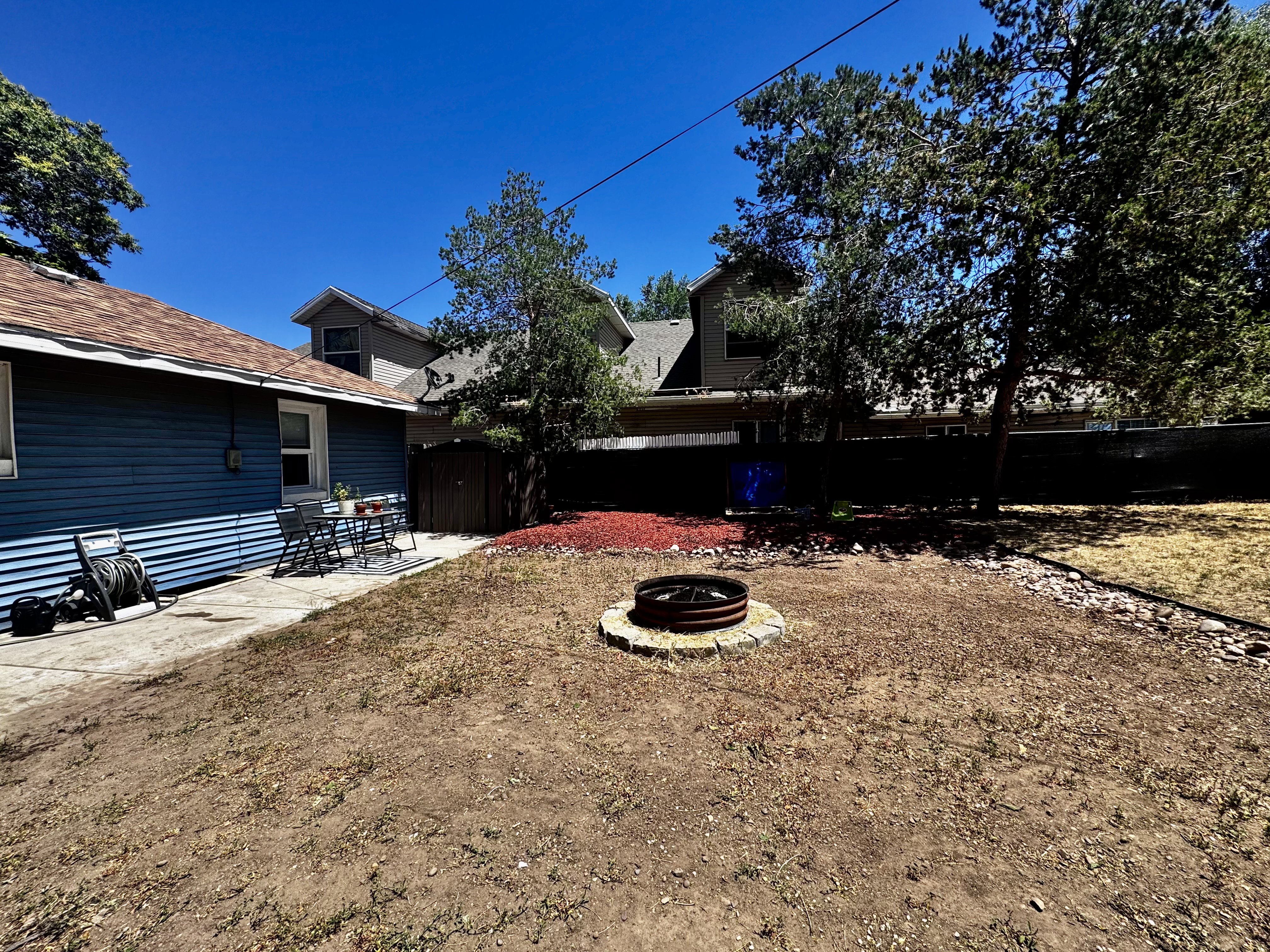 Spacious backyard featuring a concrete patio, a built-in fire pit with stone surround, a privacy fence, and mature trees
