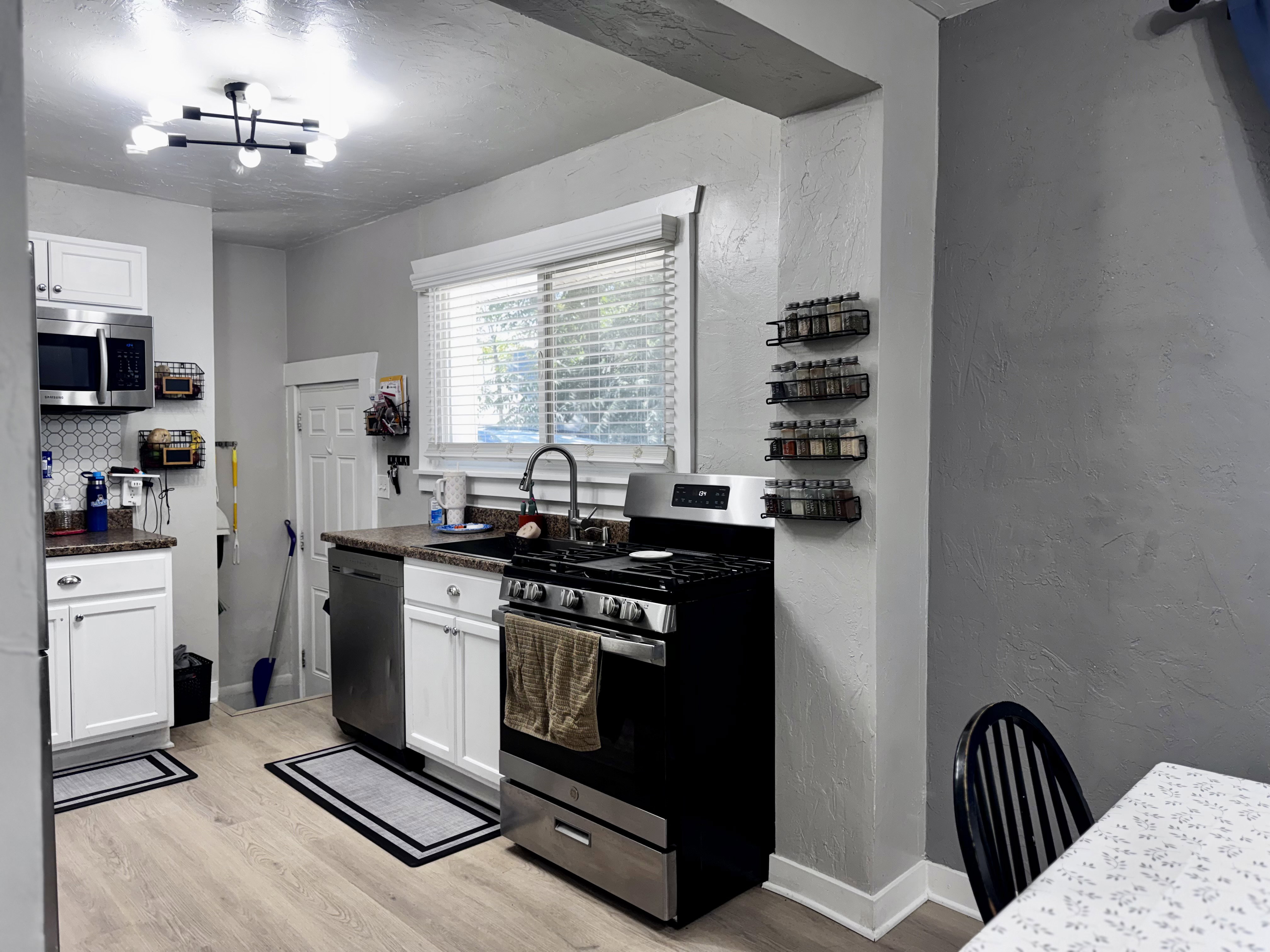 Kitchen featuring wood-finish flooring, white cabinetry, dark countertops, a hexagonal tile backsplash, and stainless steel appliances
