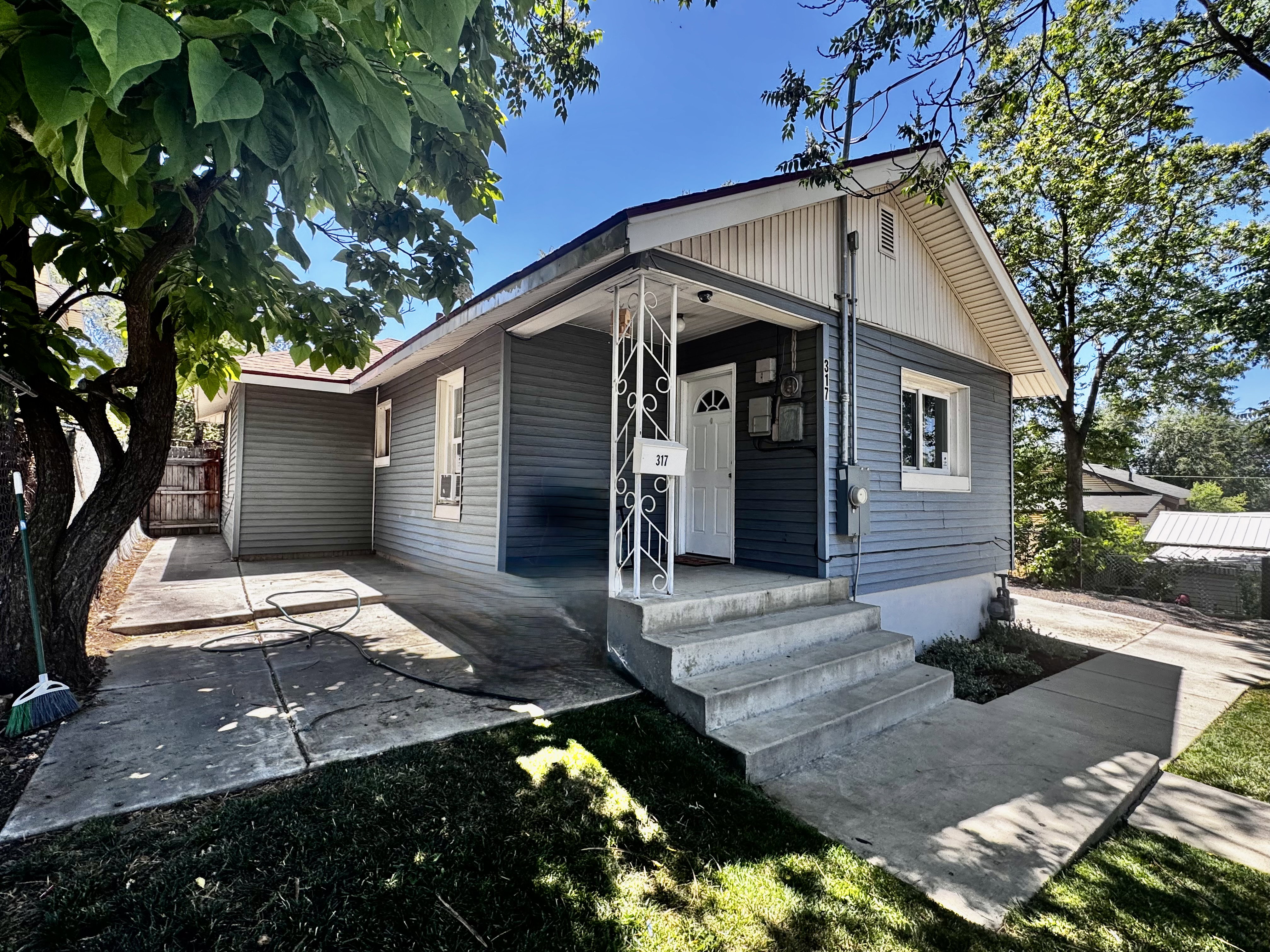 Exterior featuring blue horizontal siding, white trim, a covered front porch with white iron railings, concrete steps, and a paved driveway