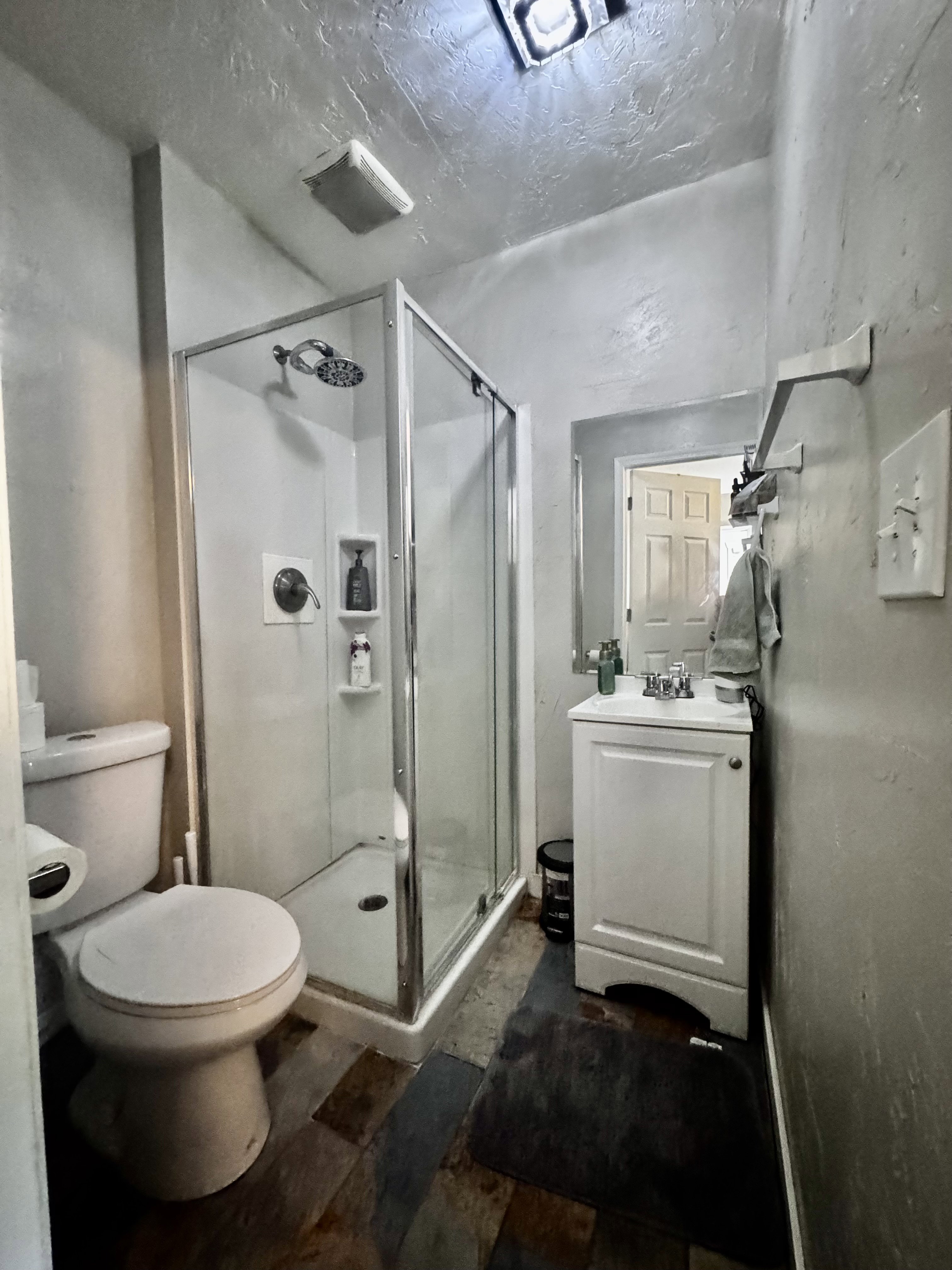 Primary Bathroom featuring a corner shower with glass enclosure, a pedestal toilet, a white single-vanity cabinet with a basin sink, and stone-look flooring