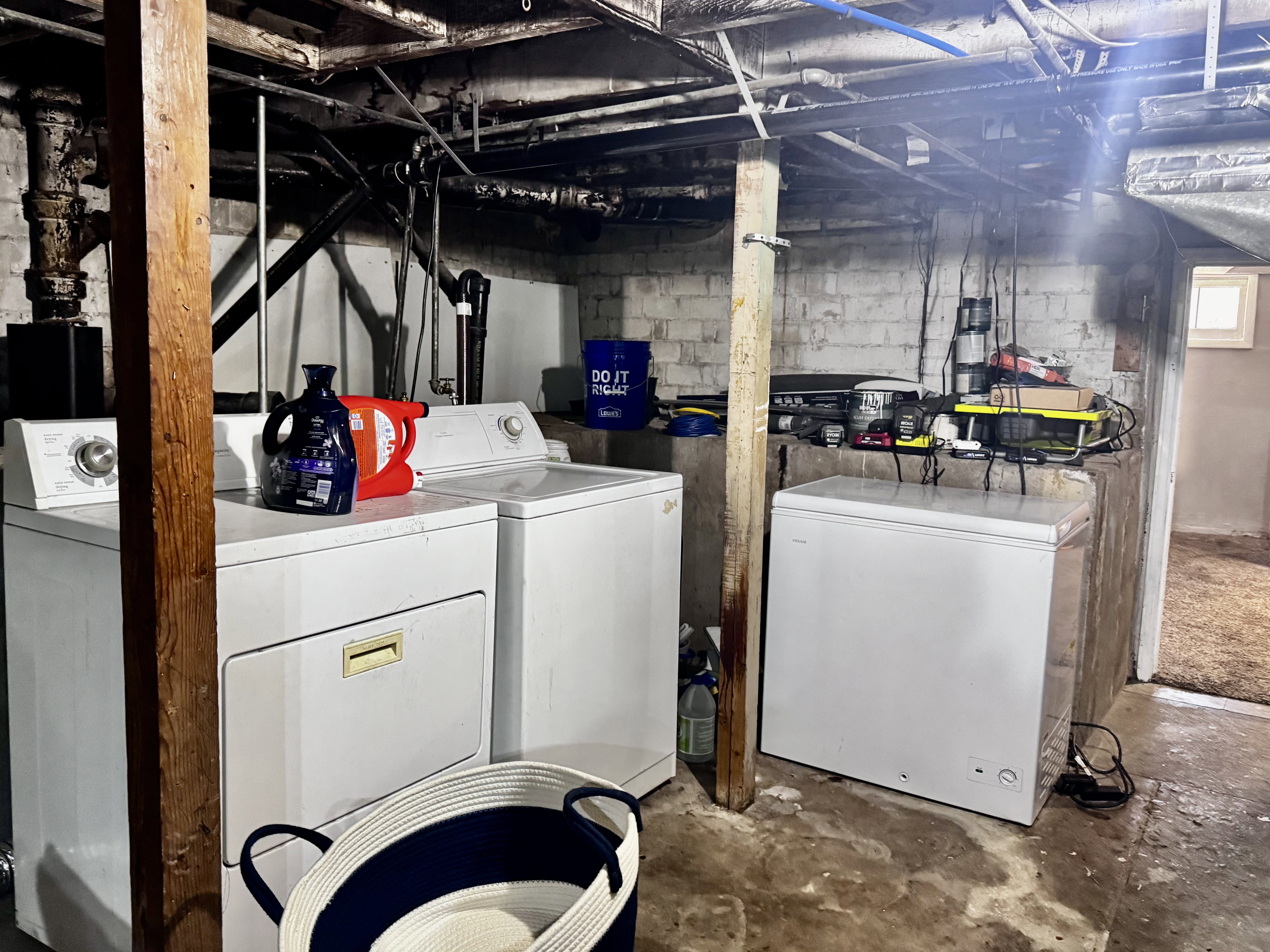 Basement utility space featuring a washer and dryer set, exposed ceiling joists, and concrete block walls