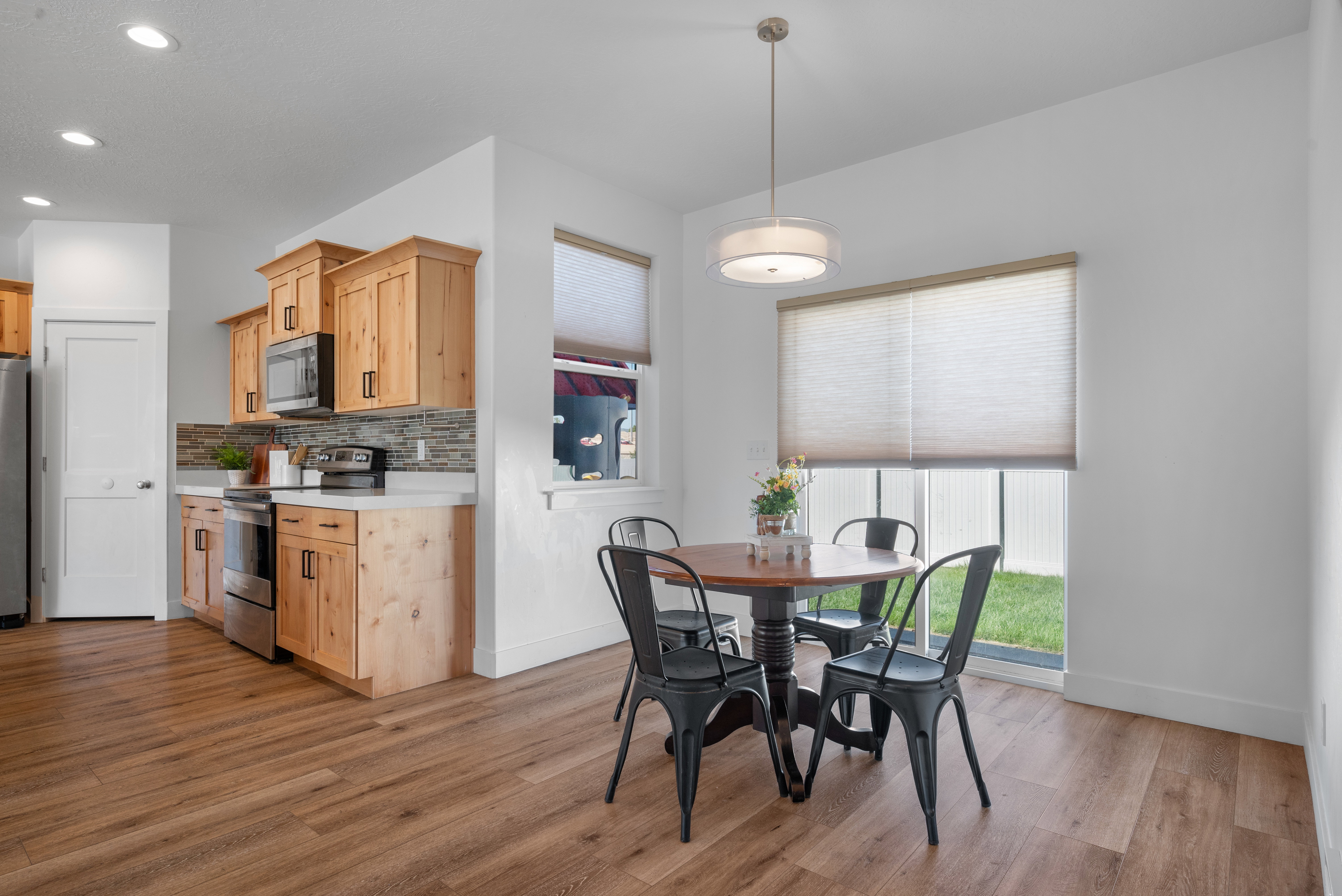 Kitchen and dining area featuring wood-finish flooring, light-toned cabinetry, stainless steel appliances, a tiled backsplash, and recessed lighting