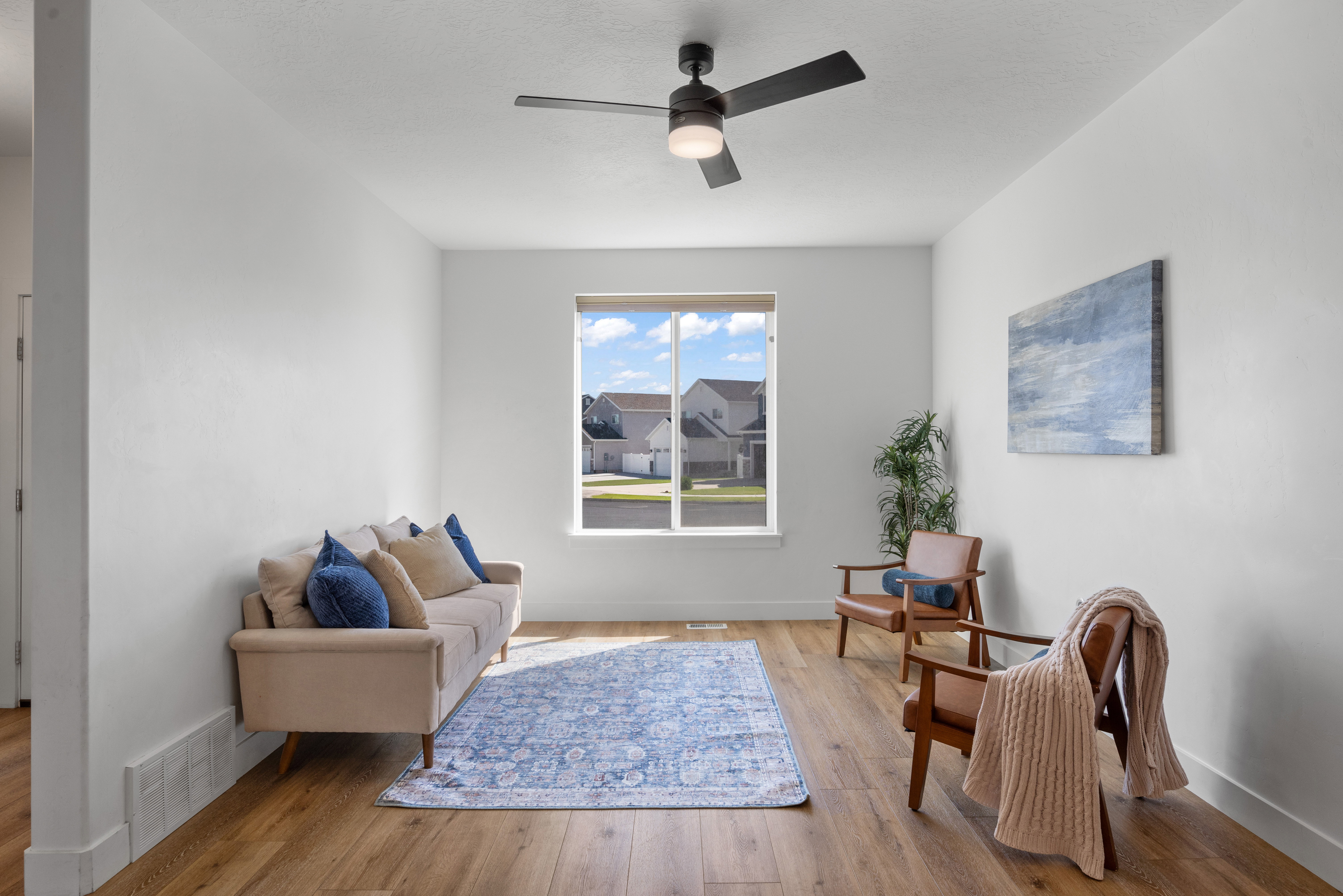 Bright living area featuring wood-finish flooring, white walls, and a large window with white trim