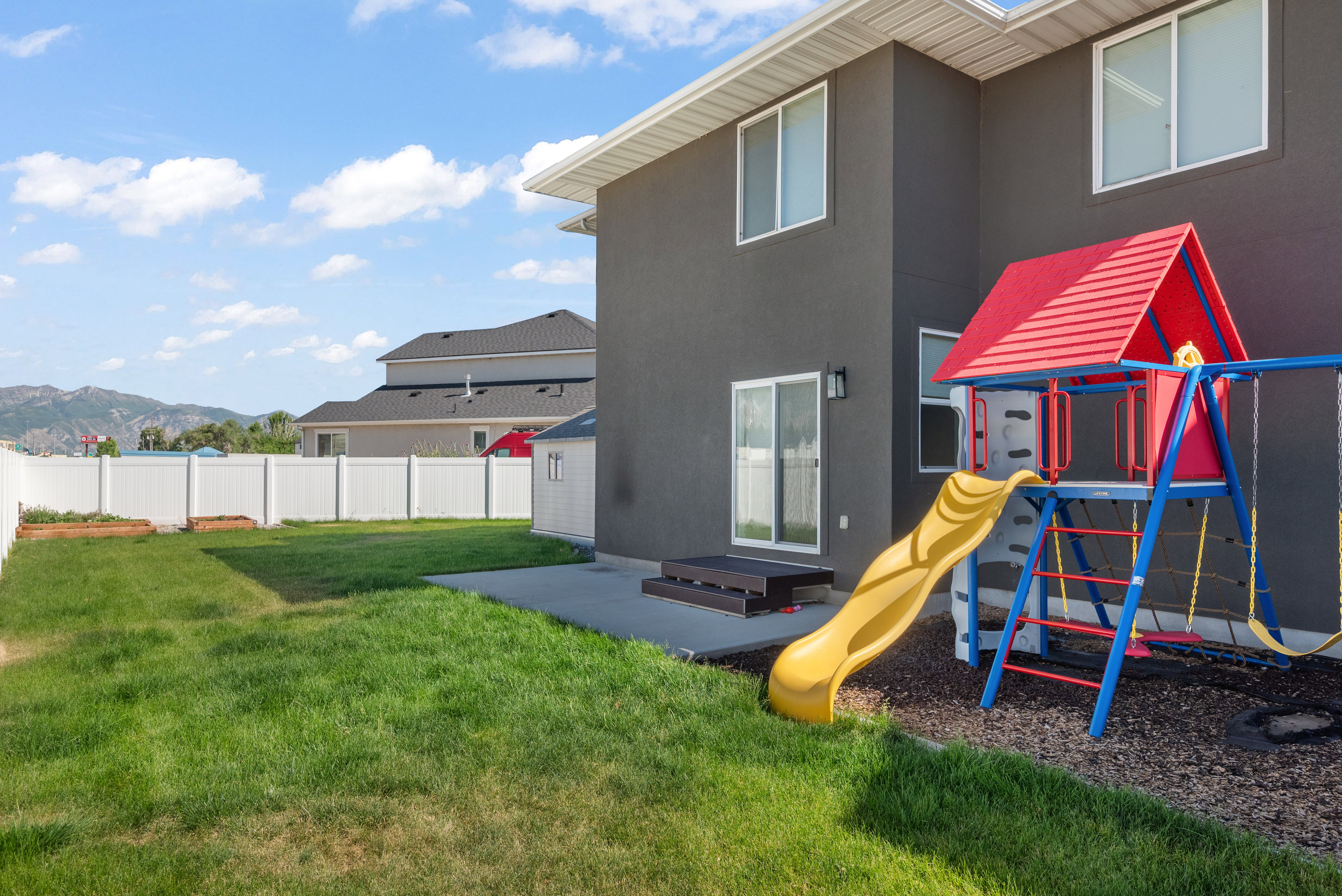 Expansive backyard with a manicured lawn, a full white vinyl privacy fence, and a concrete patio