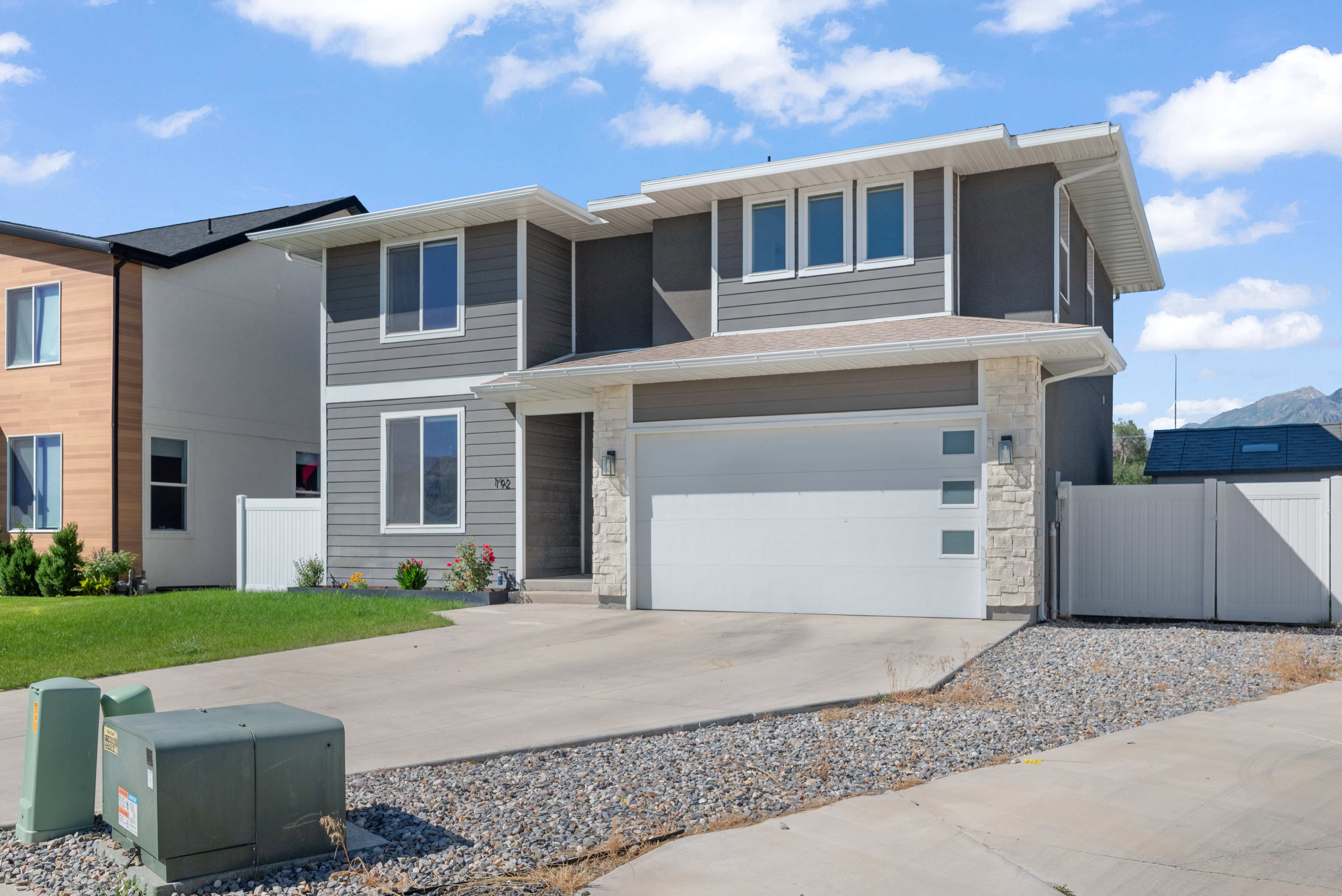 Modern two-story residence featuring a gray siding facade with white trim accents and a white garage door