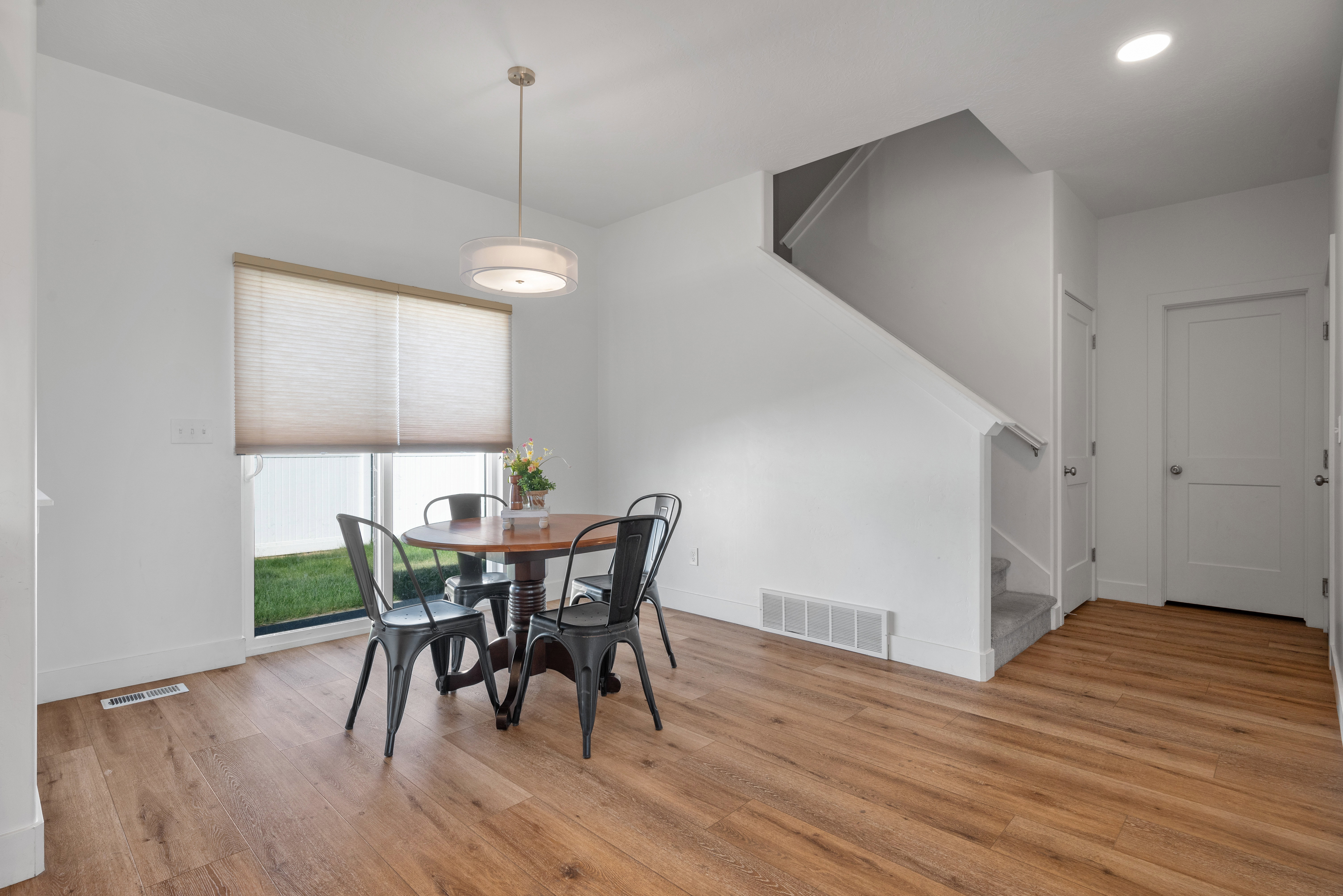 Open-concept space featuring wood-finish flooring, a contemporary drum pendant light, and a large window with privacy blinds