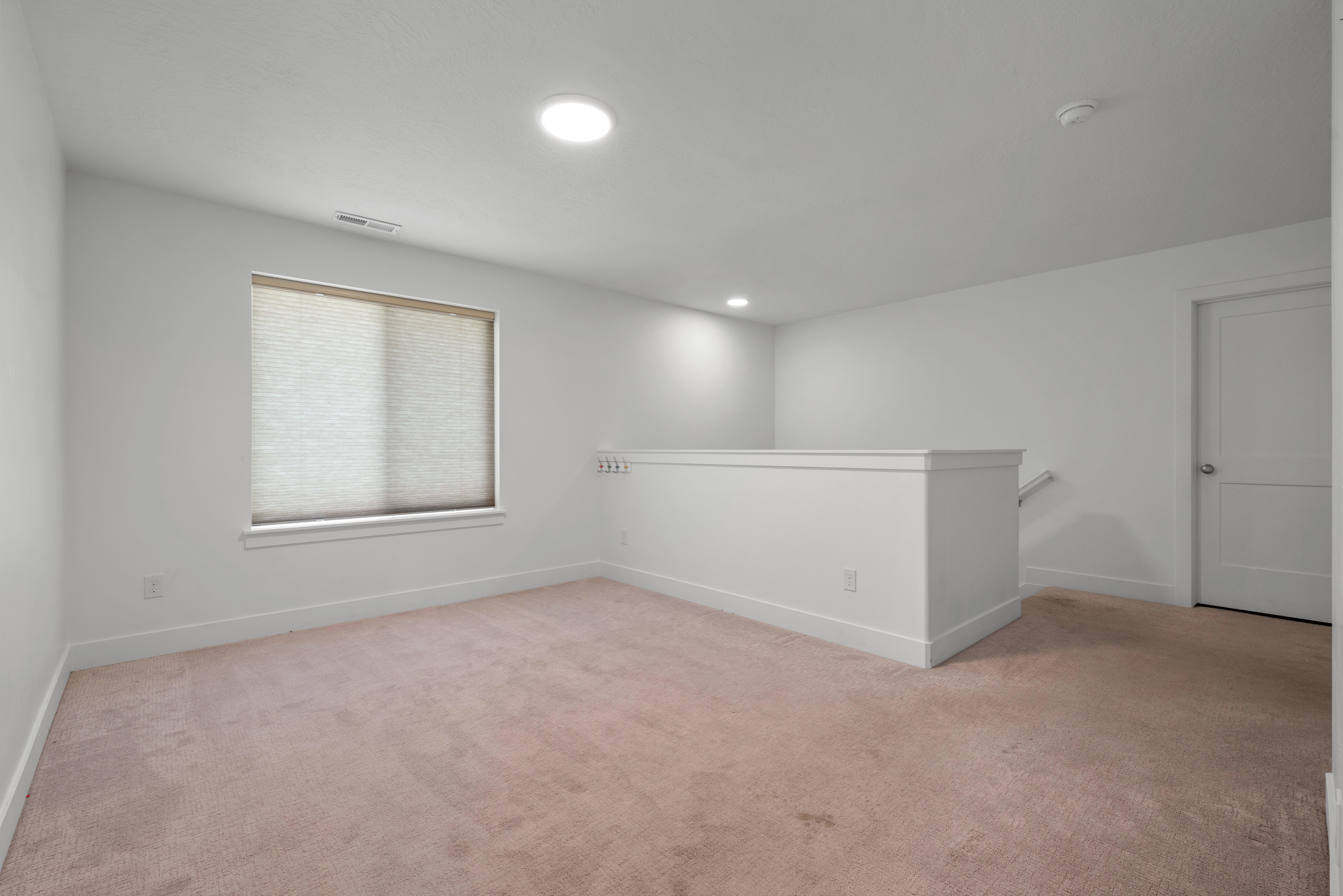 Spacious loft area featuring light-colored carpeting, a window with a cellular shade, recessed lighting, and a white interior door