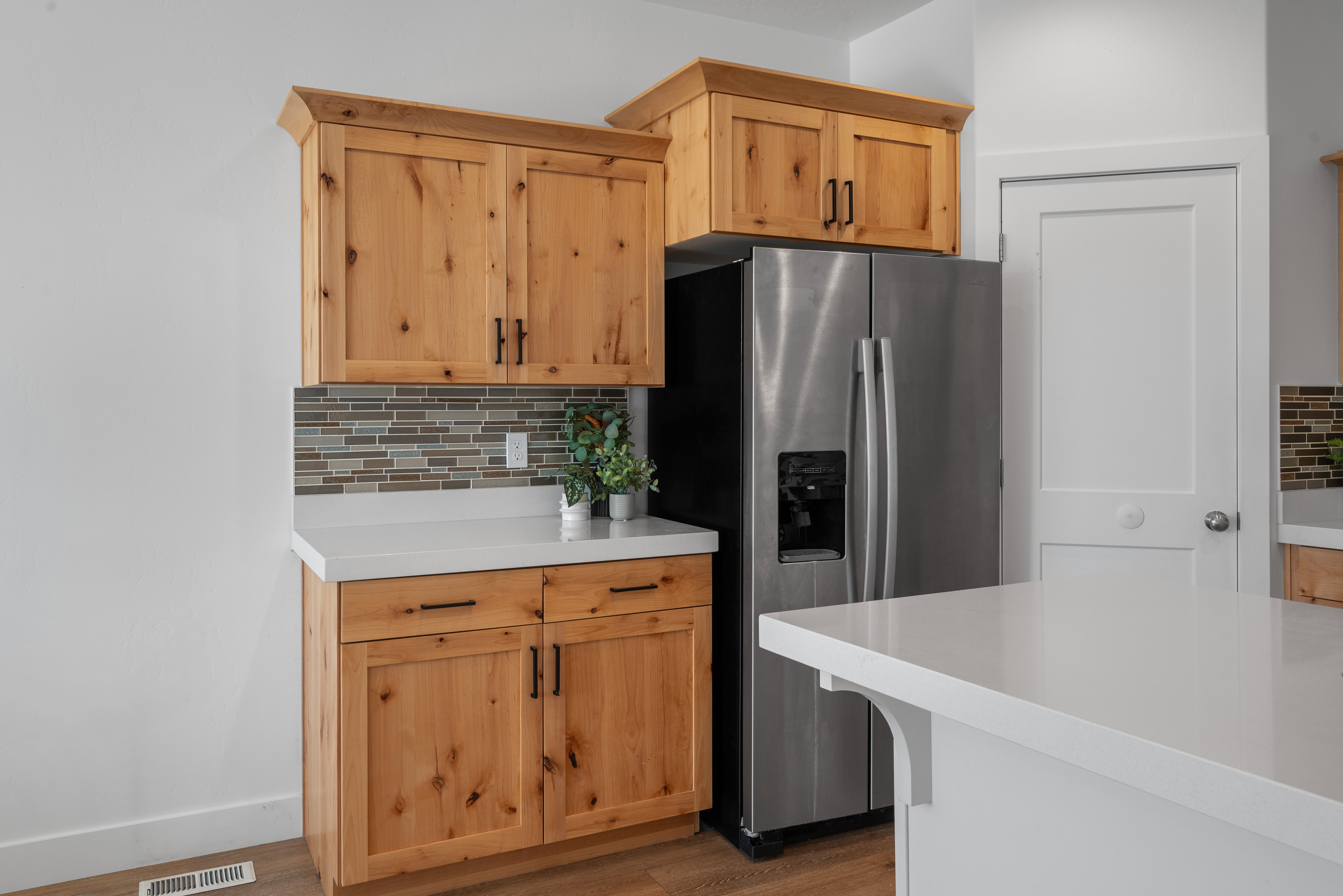 Kitchen area featuring natural wood cabinetry, stainless steel refrigerator, white countertops, and a patterned backsplash