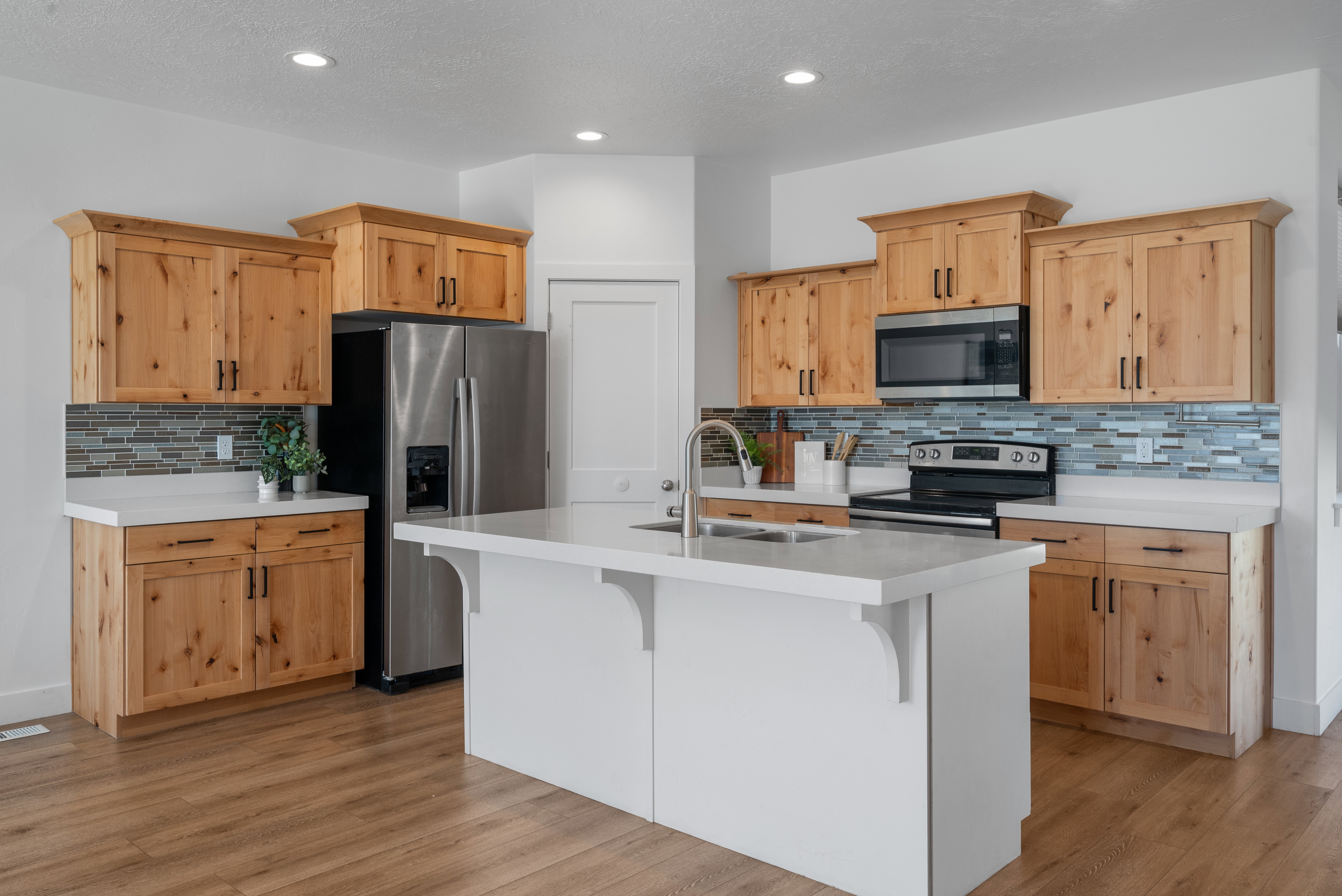 Kitchen featuring wood-finish cabinetry, stainless steel appliances, a center island with sink, quartz countertops, and a glass tile backsplash