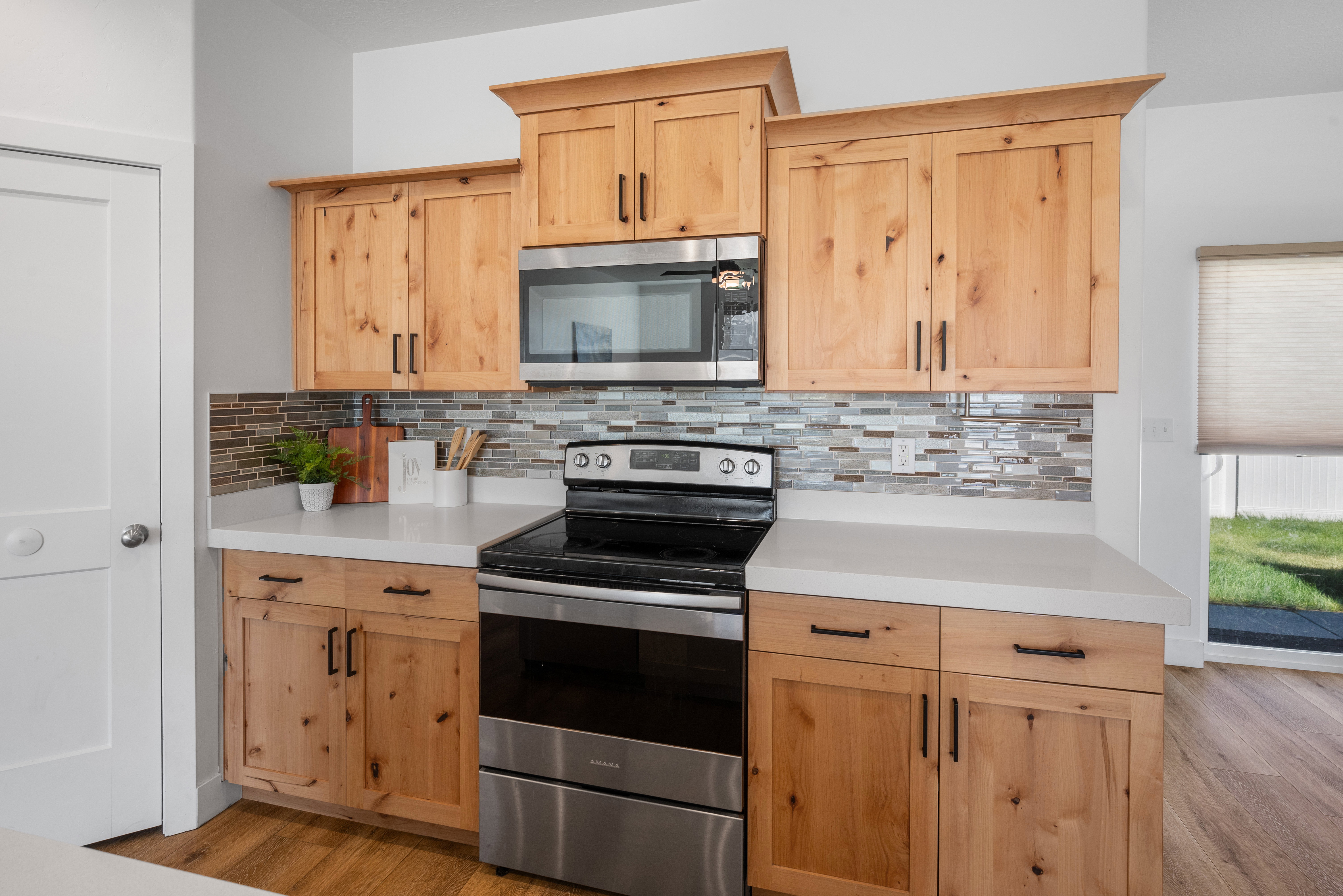Kitchen featuring natural wood-finish cabinetry, stainless steel appliances, a mosaic tile backsplash, and light-toned countertops
