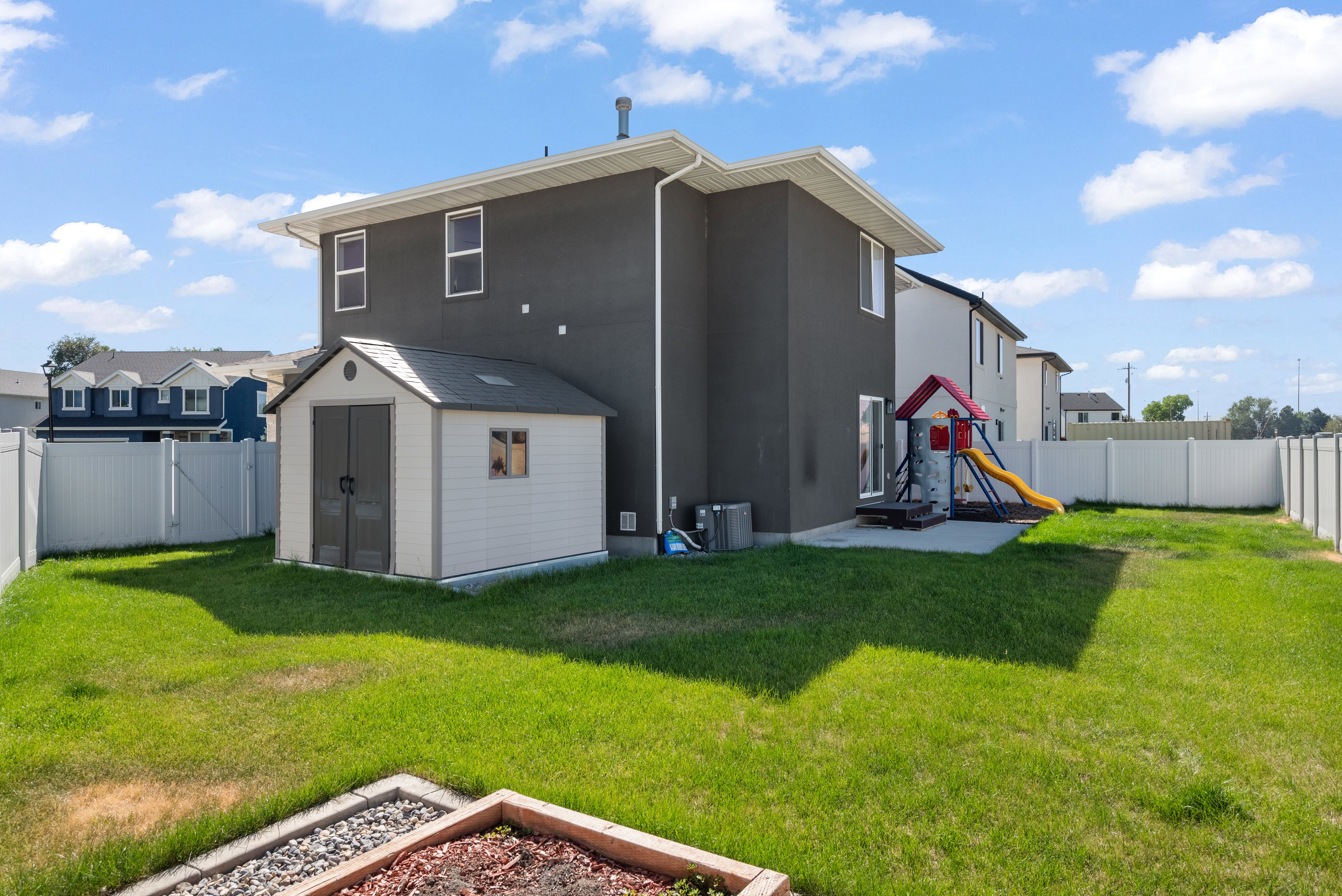 Expansive backyard featuring a manicured lawn, white privacy fencing, and a built-in storage shed