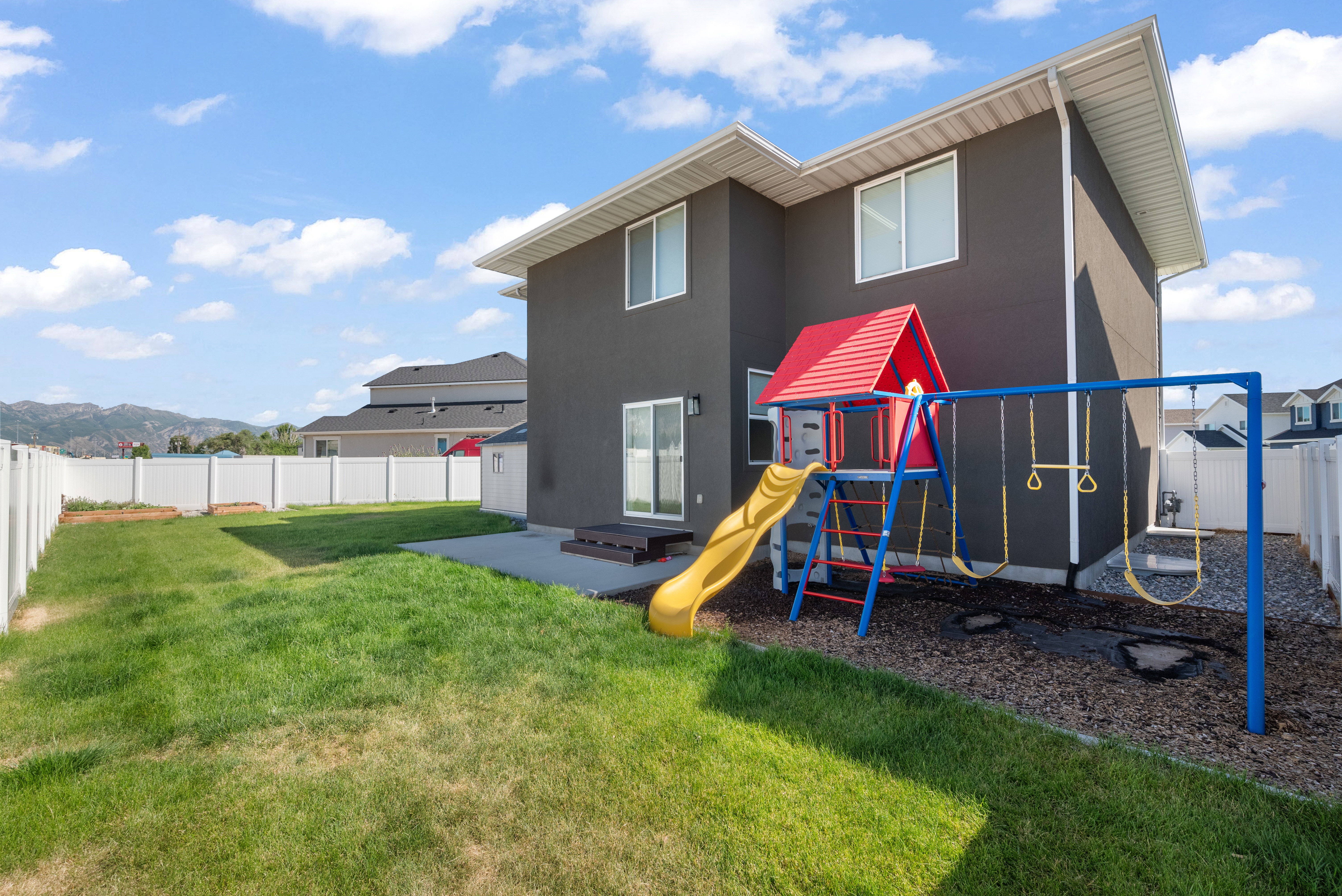 Expansive backyard featuring a manicured lawn, concrete patio, and white vinyl perimeter fencing
