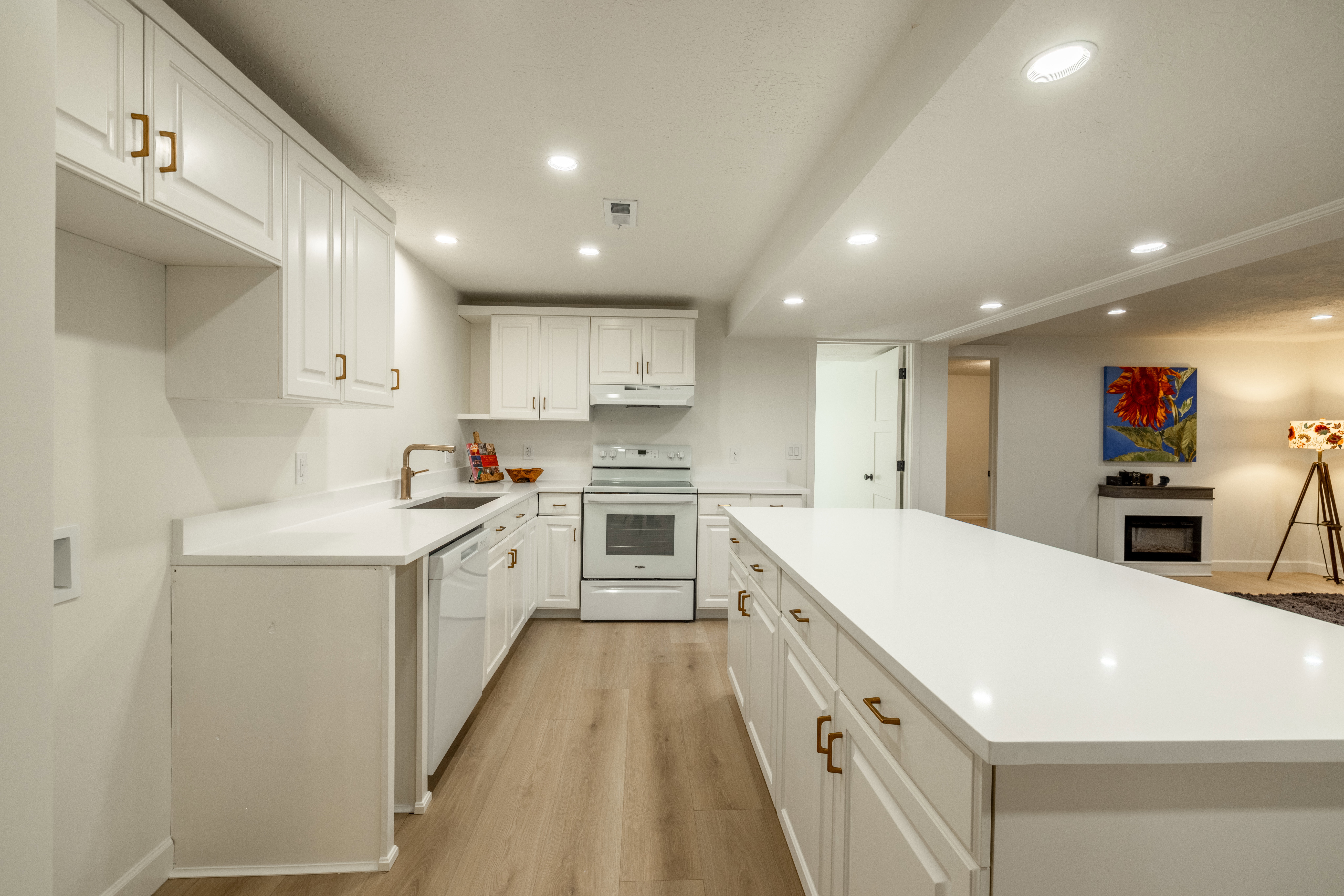 Contemporary kitchen featuring white cabinetry, bronze hardware, light-finish flooring, recessed lighting, and an extended island with a white countertop