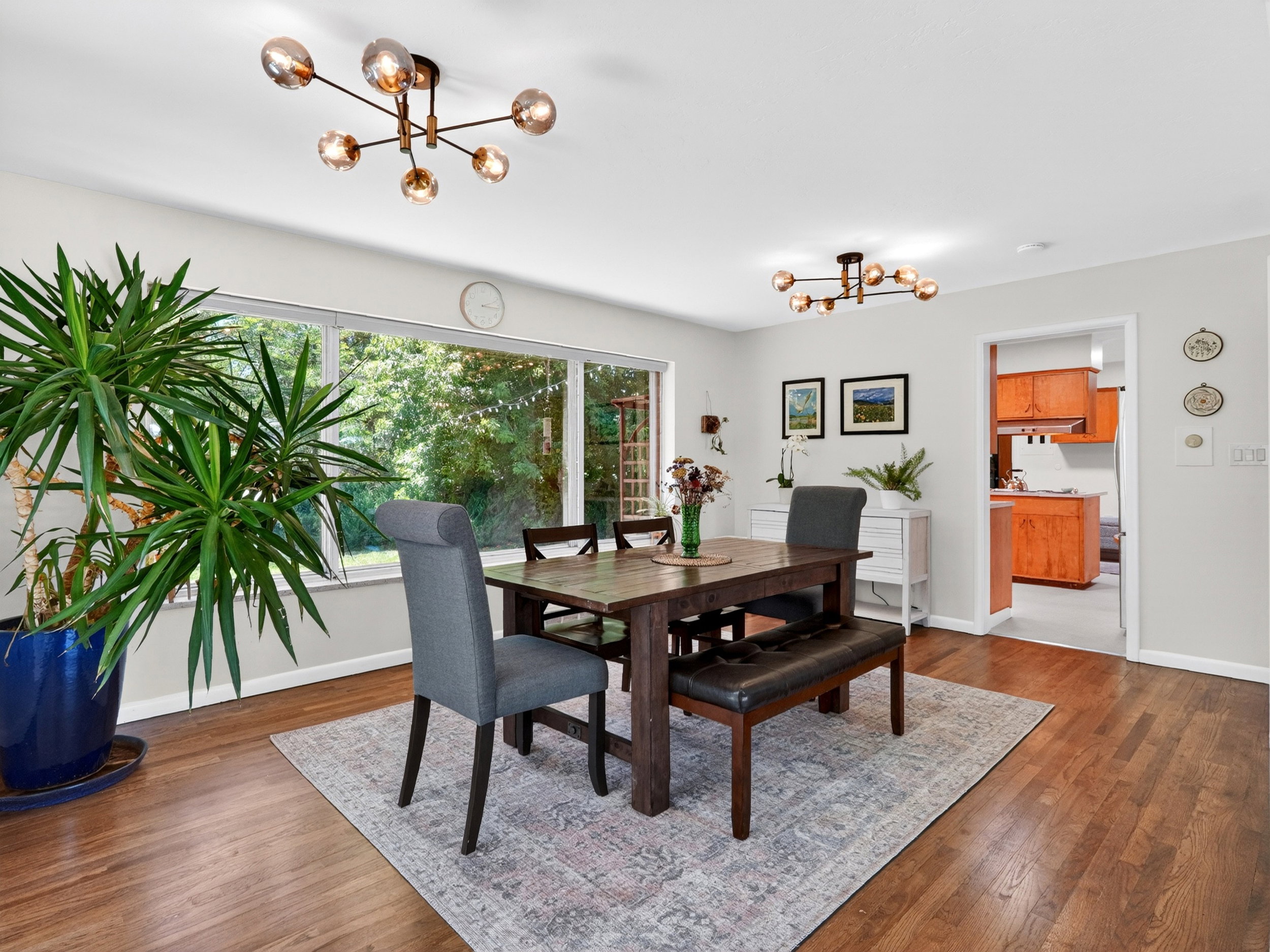 Open-concept dining area featuring wood-finish flooring, a contemporary ceiling light fixture, and a large window overlooking the backyard
