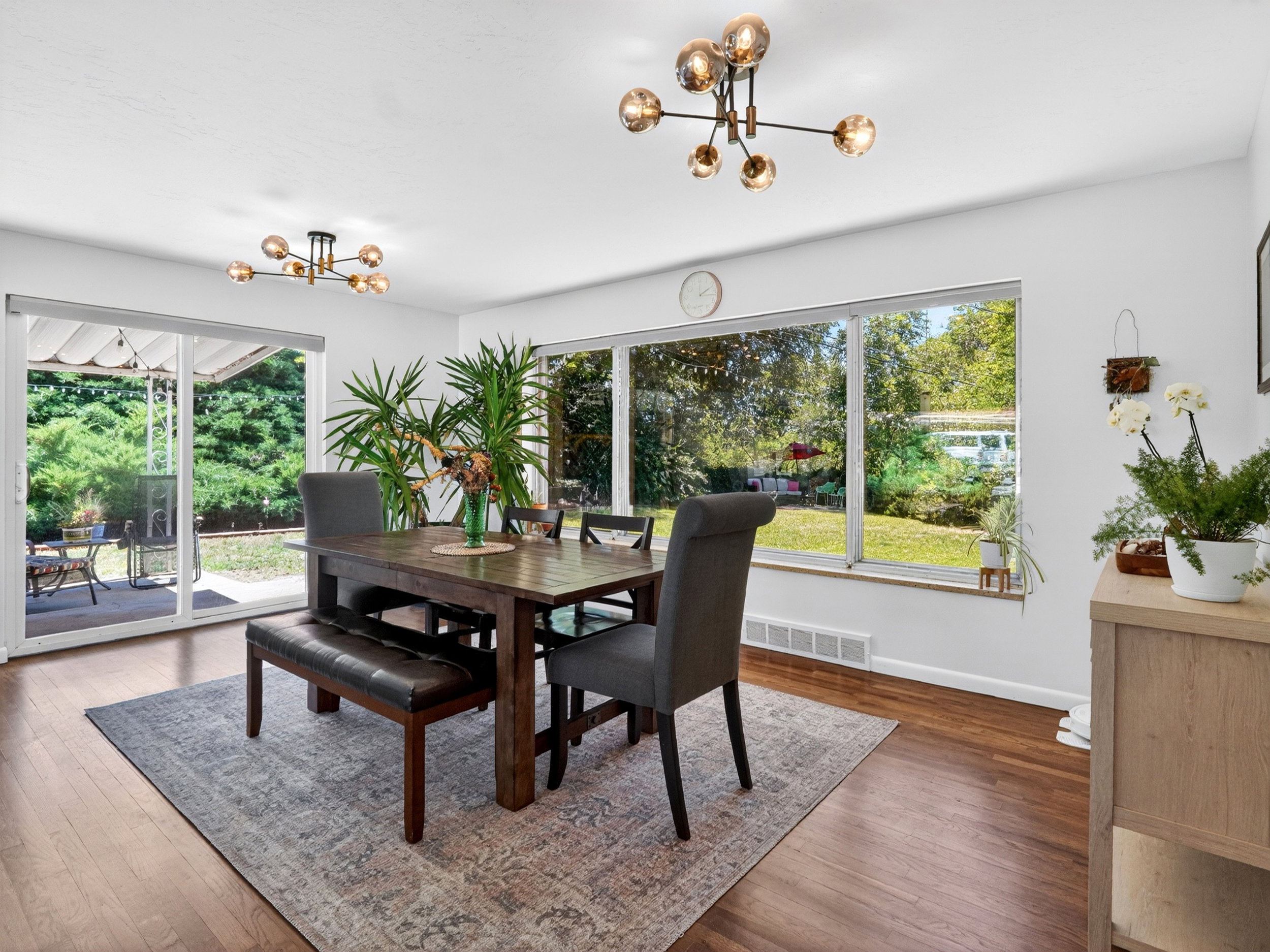 Open-concept dining area featuring wood-finish flooring, a contemporary ceiling light fixture, and a large window overlooking the backyard