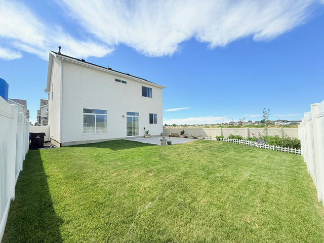 Expansive rear yard featuring a manicured lawn, a white privacy fence, and a concrete patio