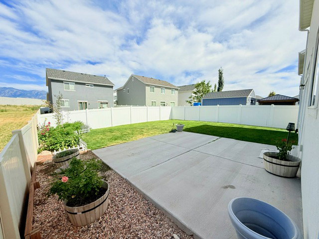 Spacious backyard featuring a concrete patio, green lawn, and white vinyl fencing