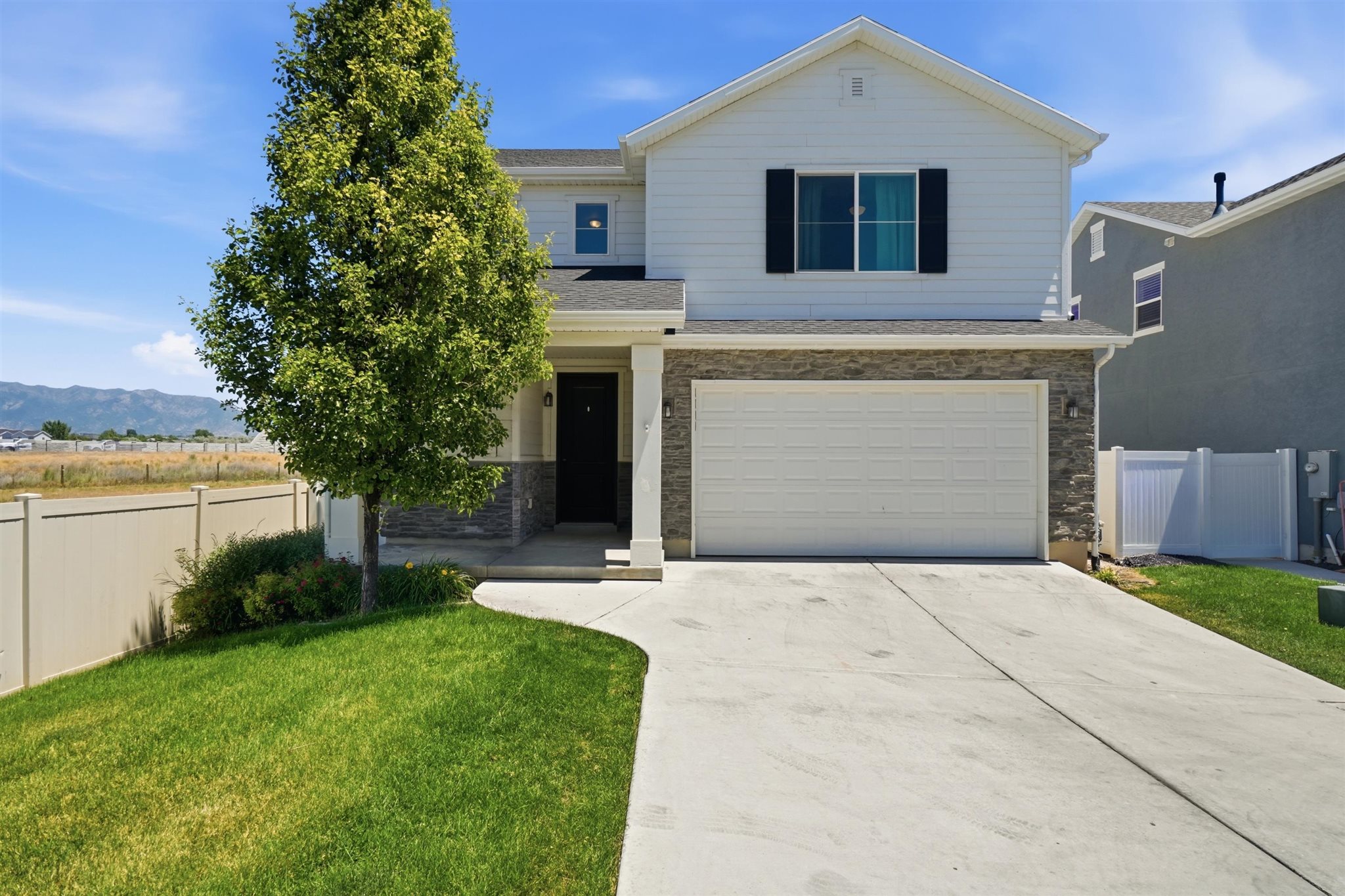 White siding exterior with stone accenting, a two-car garage, and a concrete driveway