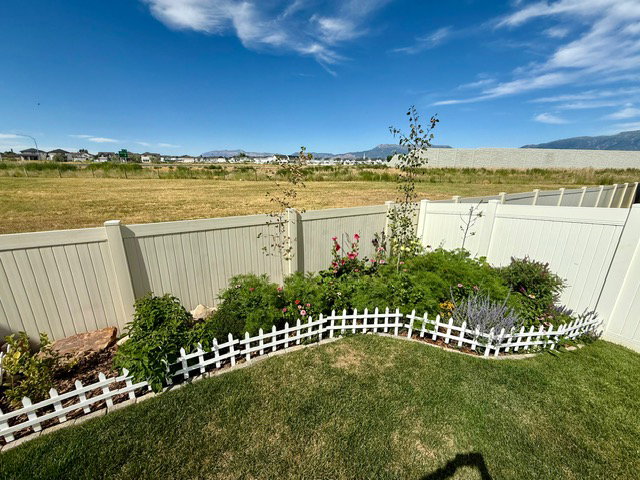 Manicured lawn with a garden bed featuring varied plantings and a decorative white picket fence border