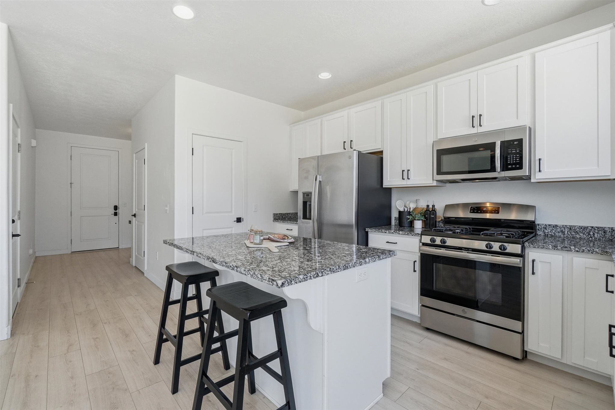 Kitchen featuring an island with seating, white shaker-style cabinetry, stainless steel appliances, granite countertops, and wood-finish flooring